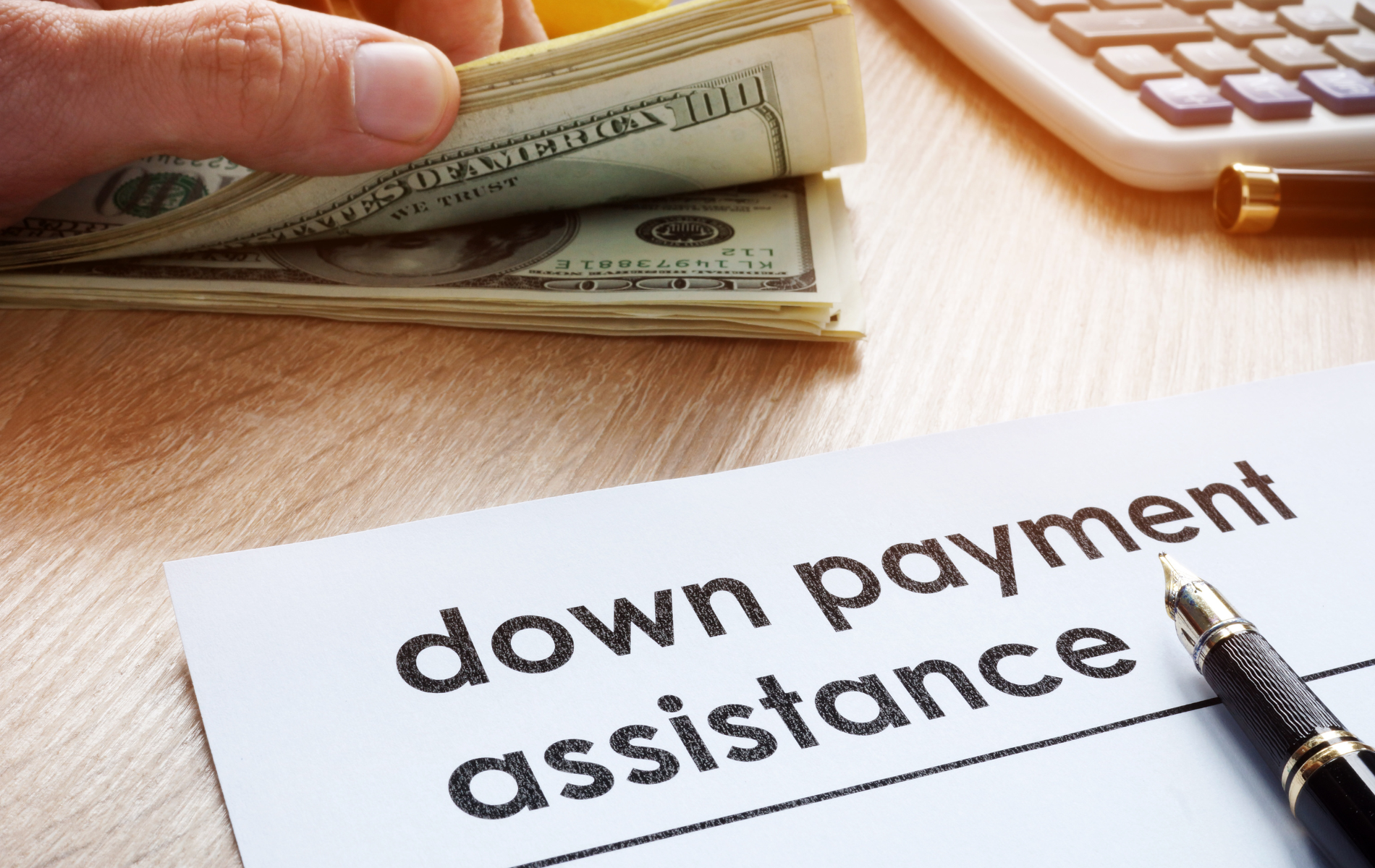 A person is holding a stack of money next to a down payment assistance form.