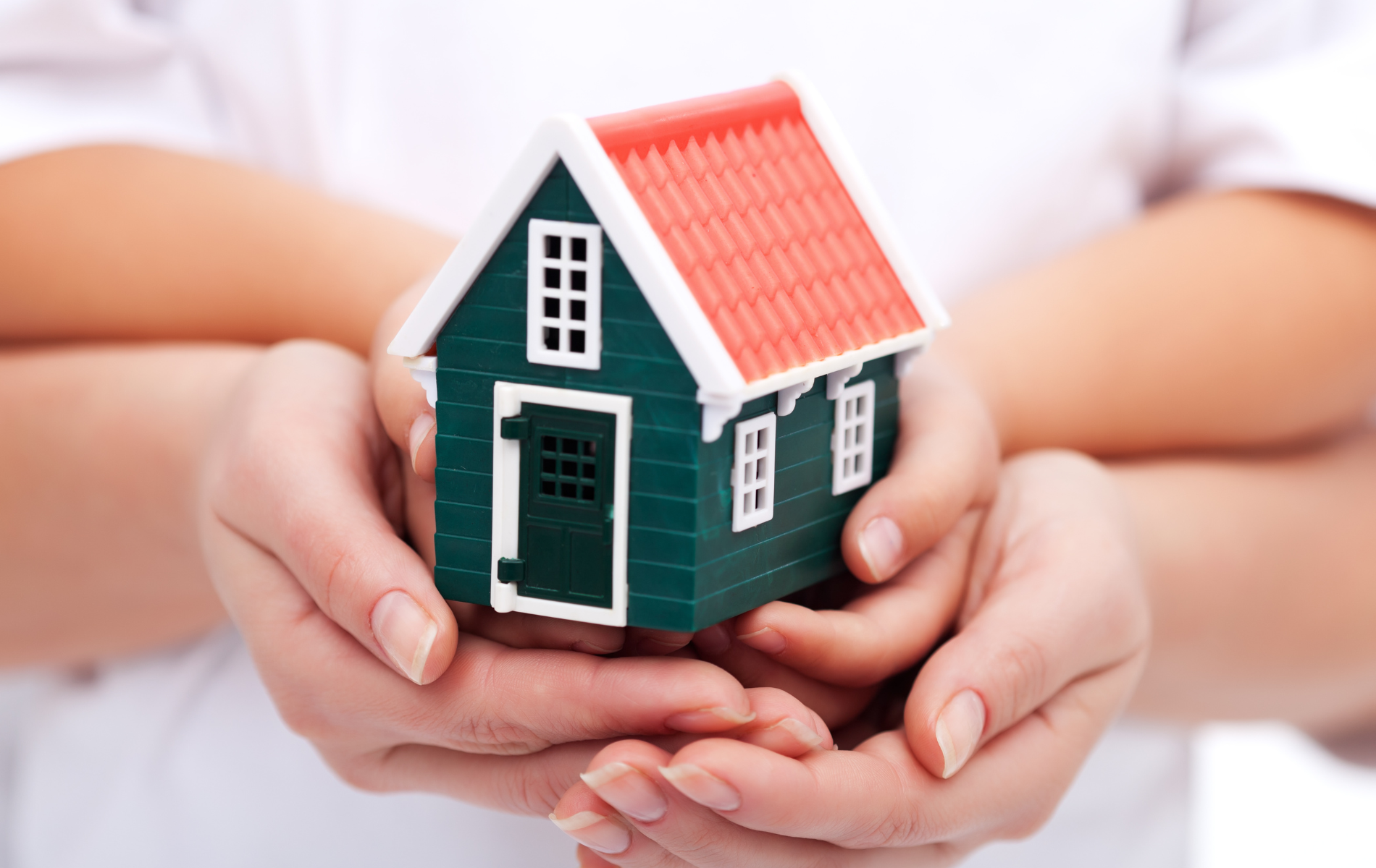 Two people are holding a small green house in their hands.