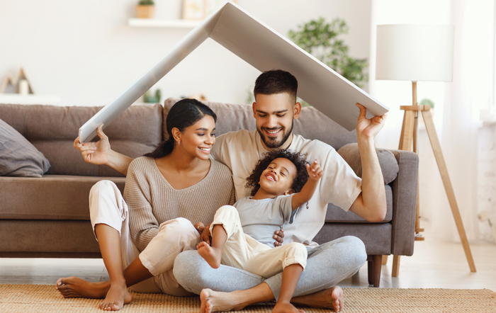 A family is sitting on the floor under a cardboard house.