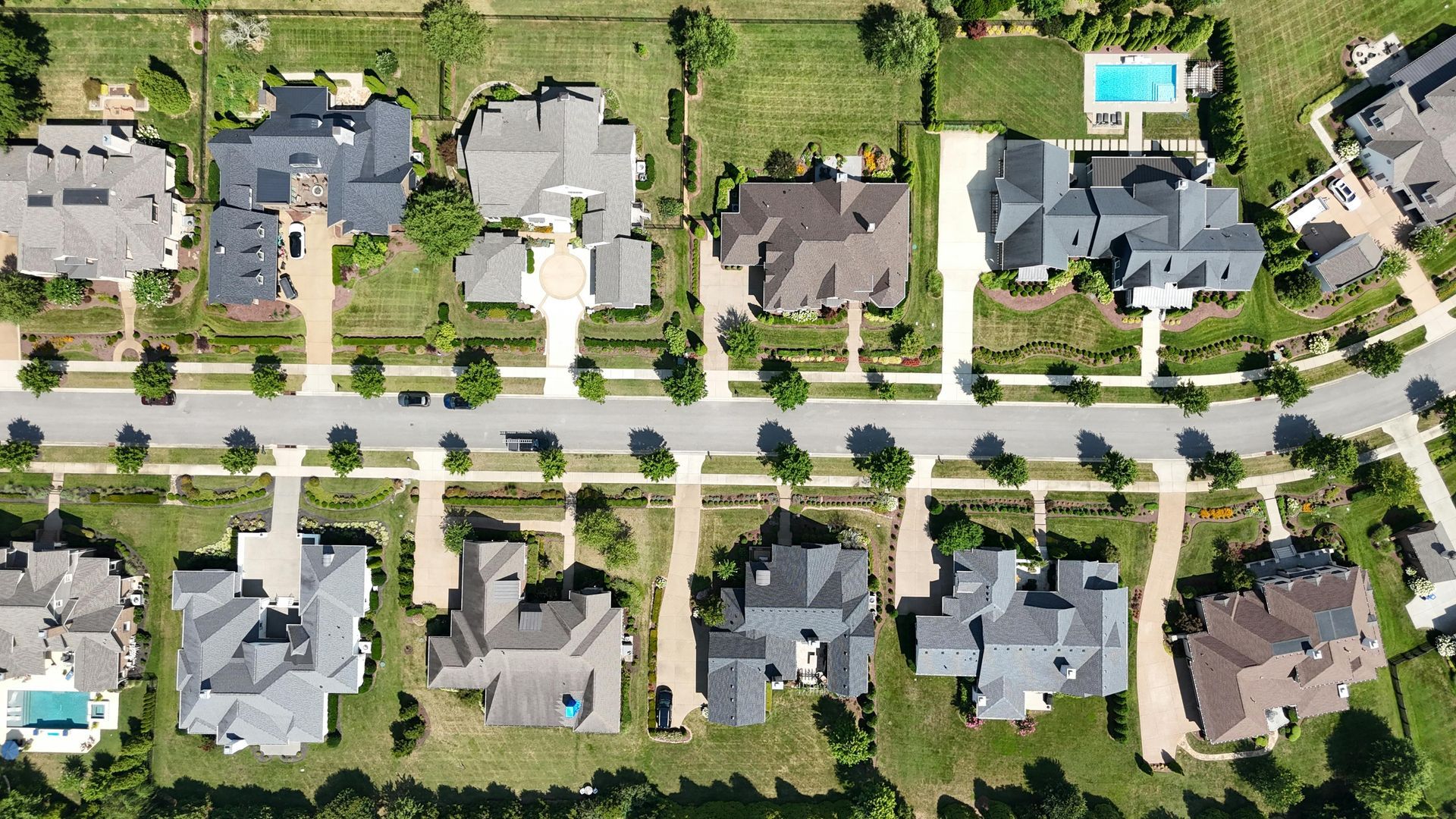 Aerial view of a suburban neighborhood with rows of houses, tree-lined streets, and a swimming pool.