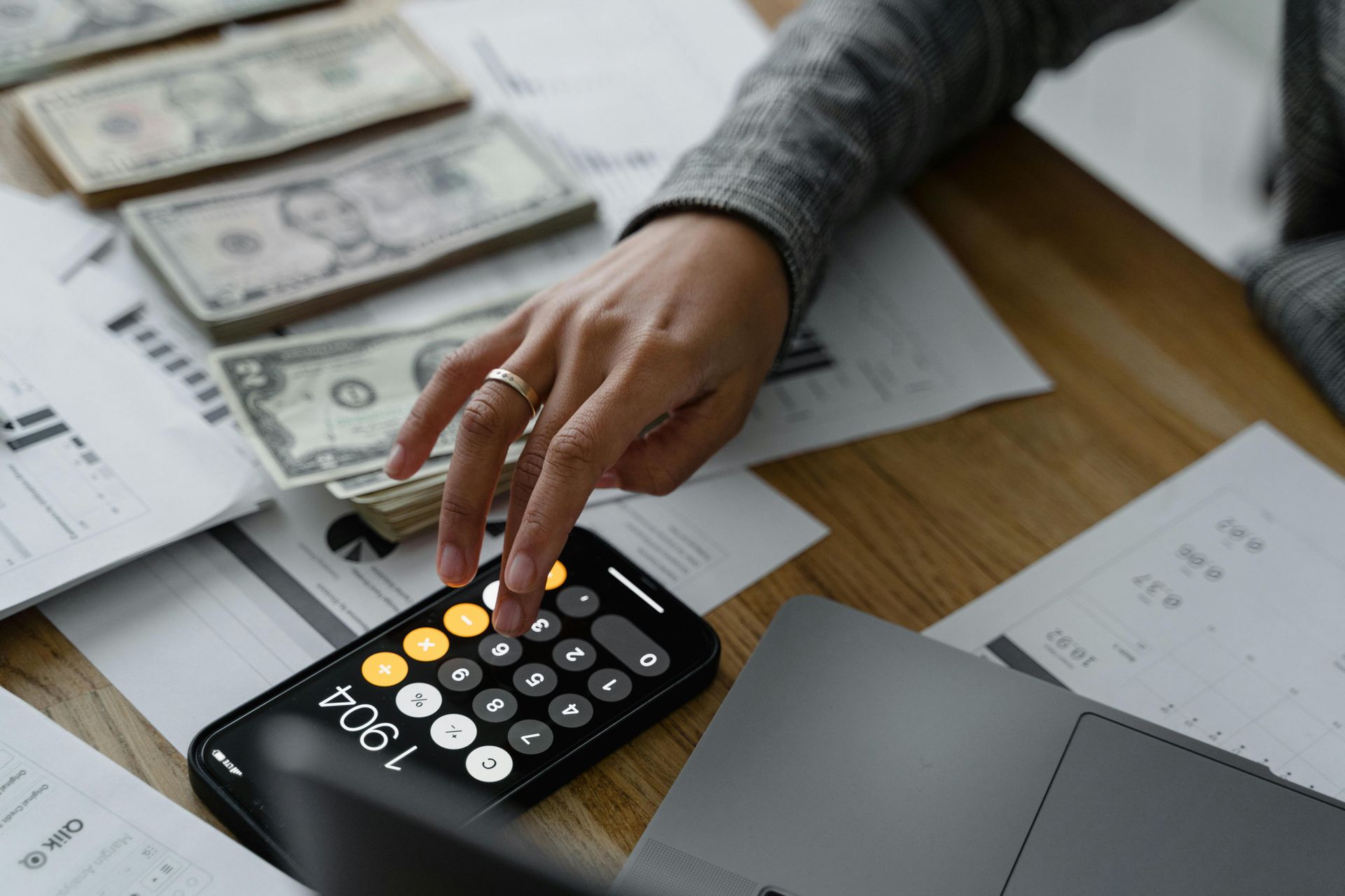 Hand using calculator beside cash and paperwork on a desk