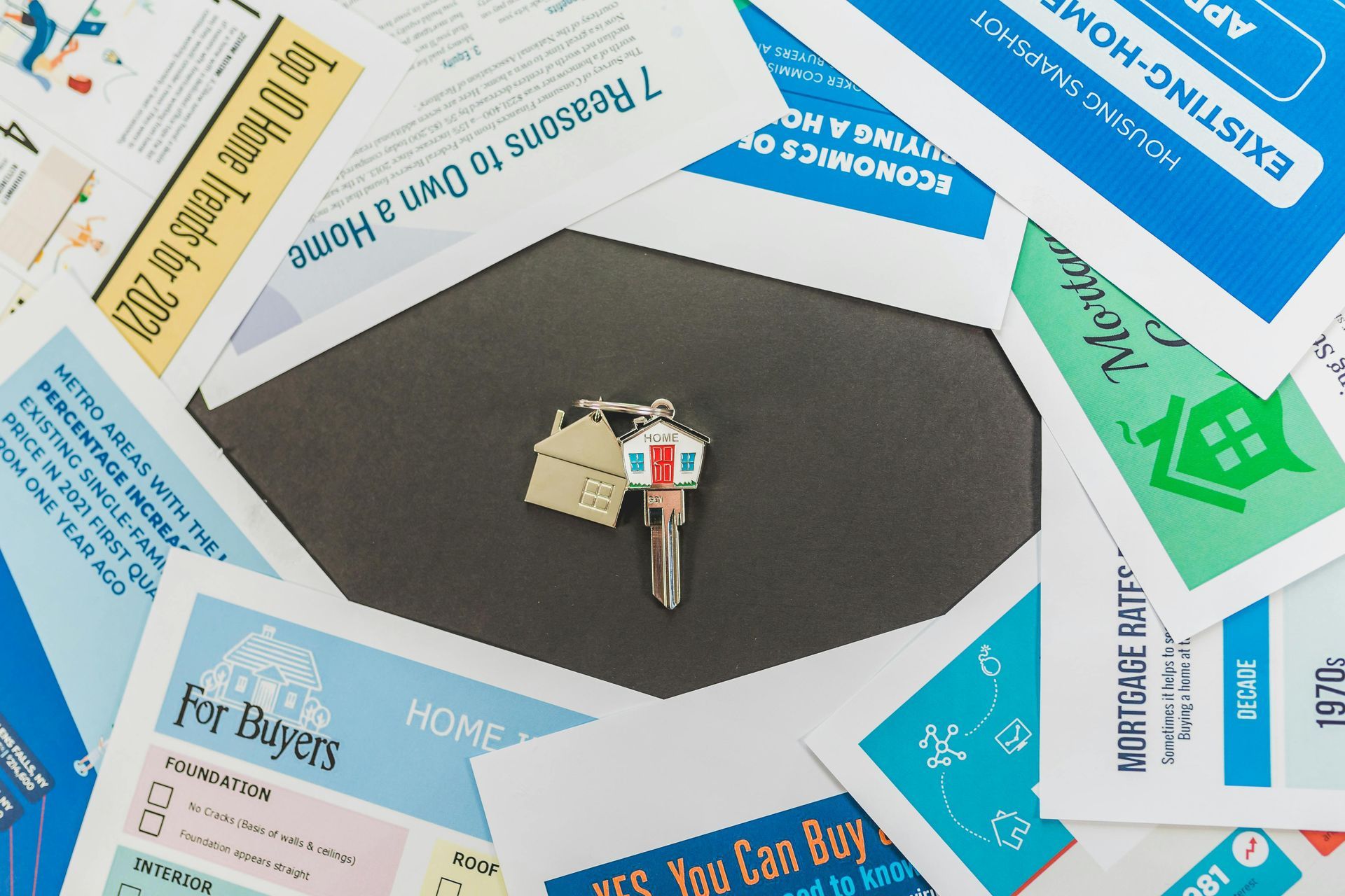 A single house-shaped key rests in the center of several overlapping informational documents about buying a home.