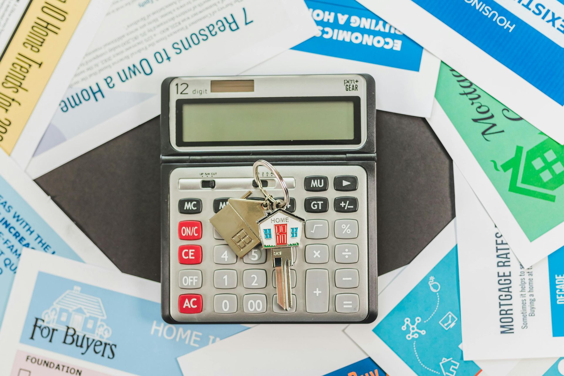 A calculator with a house-shaped keychain sits on top of various brochures about buying a home and mortgage rates.