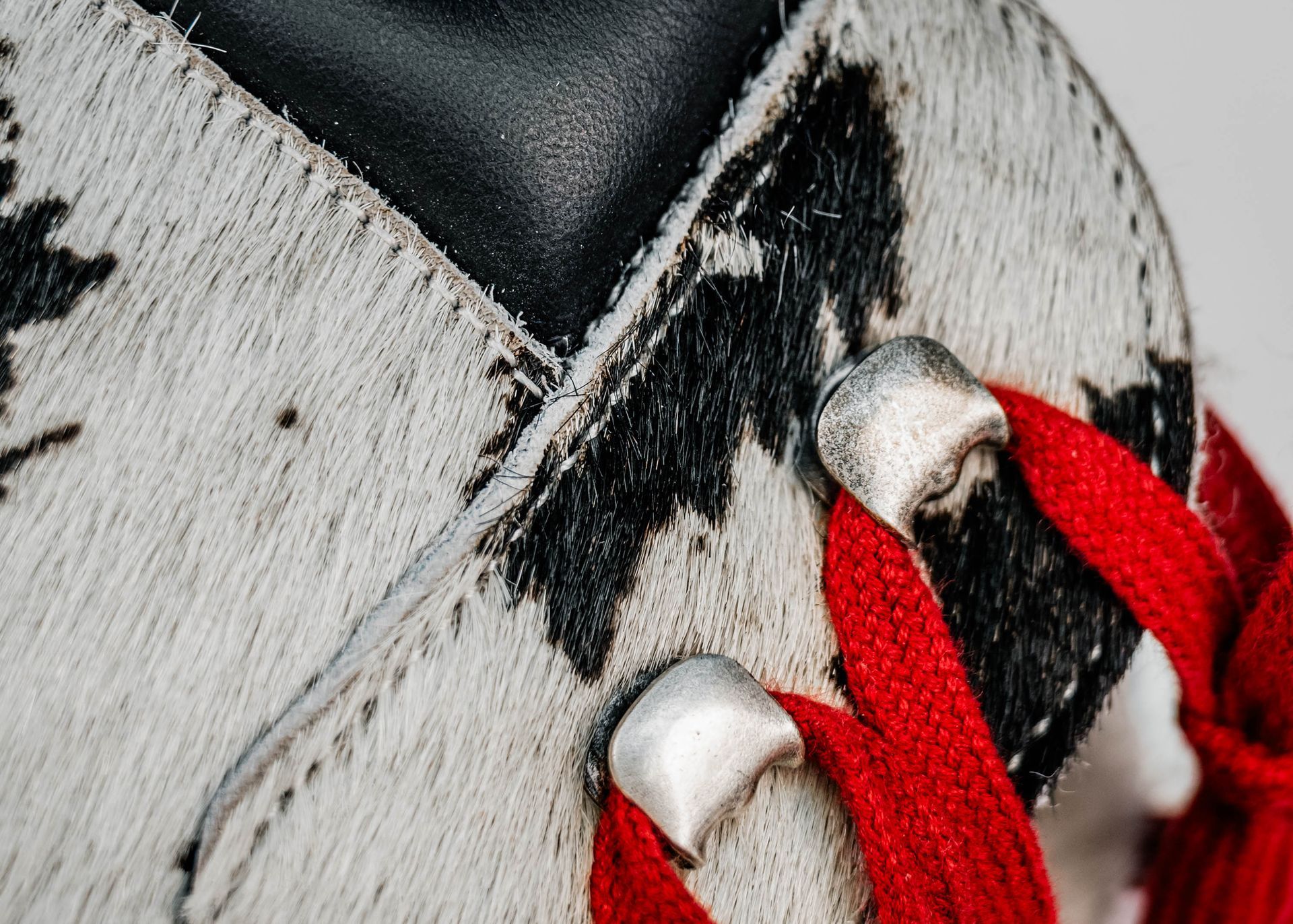 Nahaufnahme eines Schuhs mit schwarz-weiß geflecktem Obermaterial aus Fell, roten Schnürsenkeln und silbernen Metallösen.