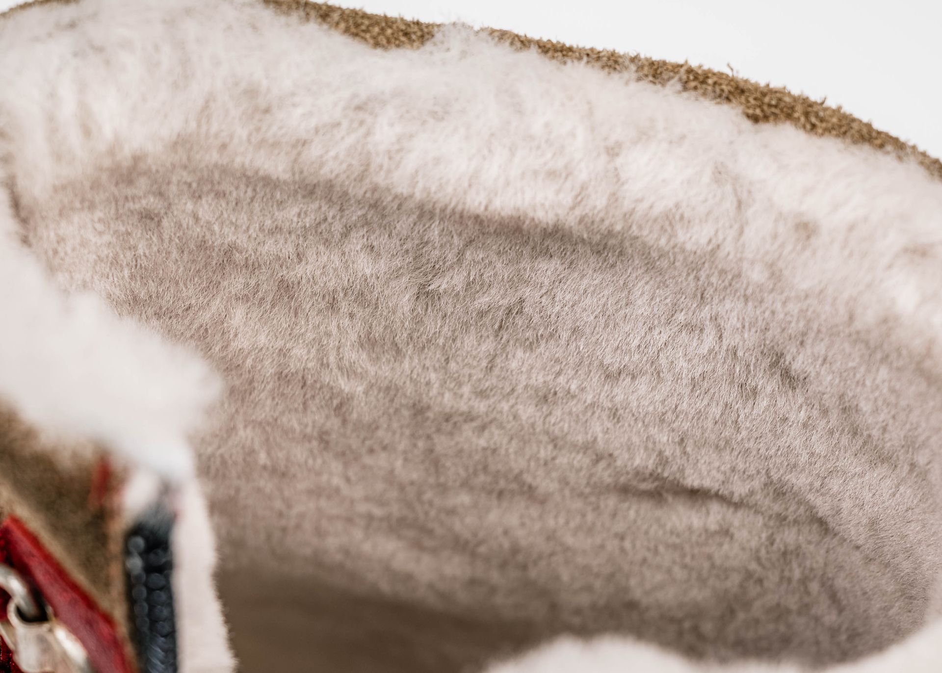 Nahaufnahme des Inneren eines Stiefels mit flauschigem weißem Wollfutter und braunem Wildleder.