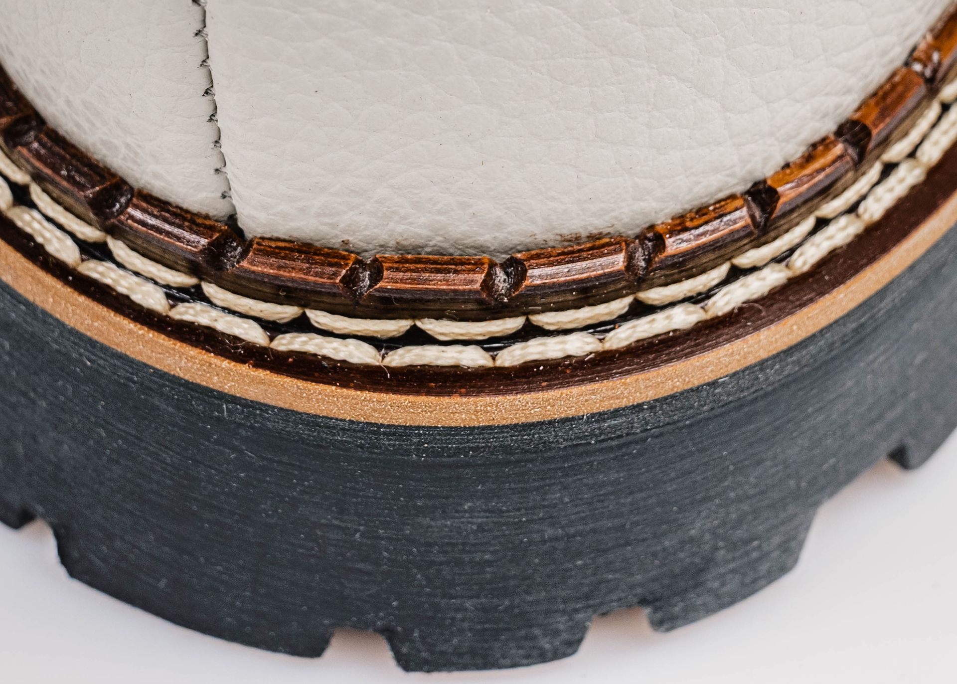 Nahaufnahme der mehrschichtigen Sohlenkonstruktion eines weißen Lederschuhs mit braunen, beigen und dunkelgrauen Elementen.