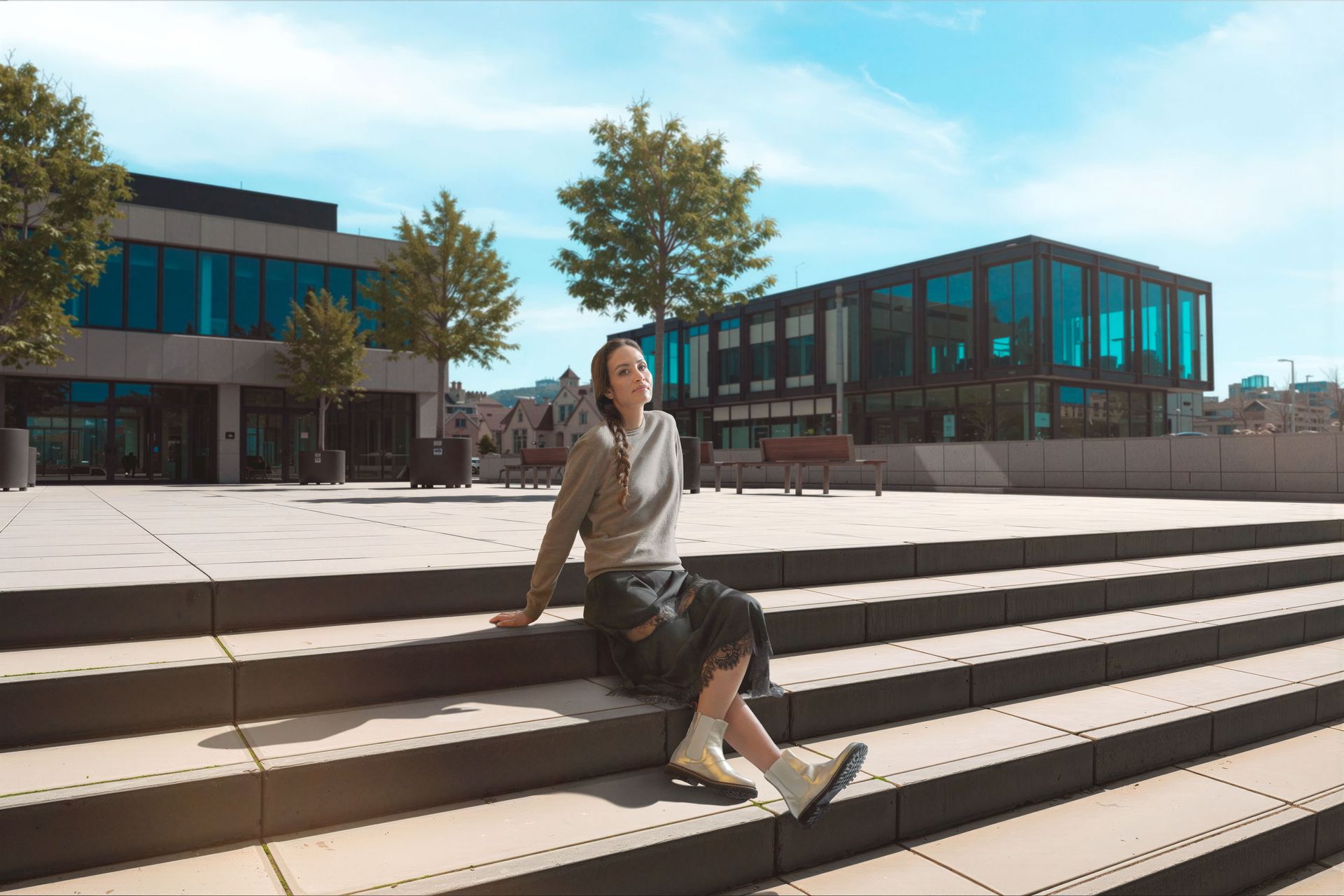Person sitzt auf Betonstufen, sonnige Außenumgebung. Gebäude im Hintergrund.
