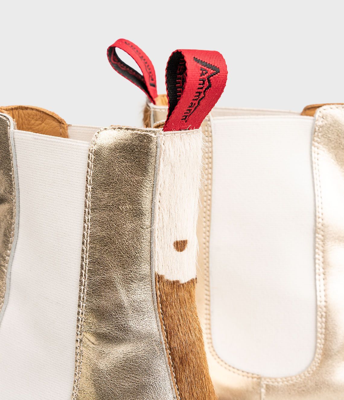 Bottines Chelsea dorées avec tirettes rouges, empiècements latéraux élastiques blancs et semelles foncées.