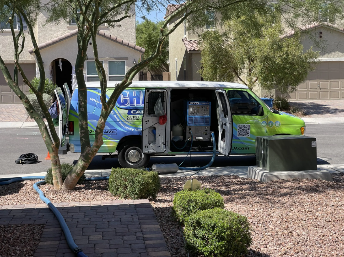 A green van is parked in front of a house with its doors open.