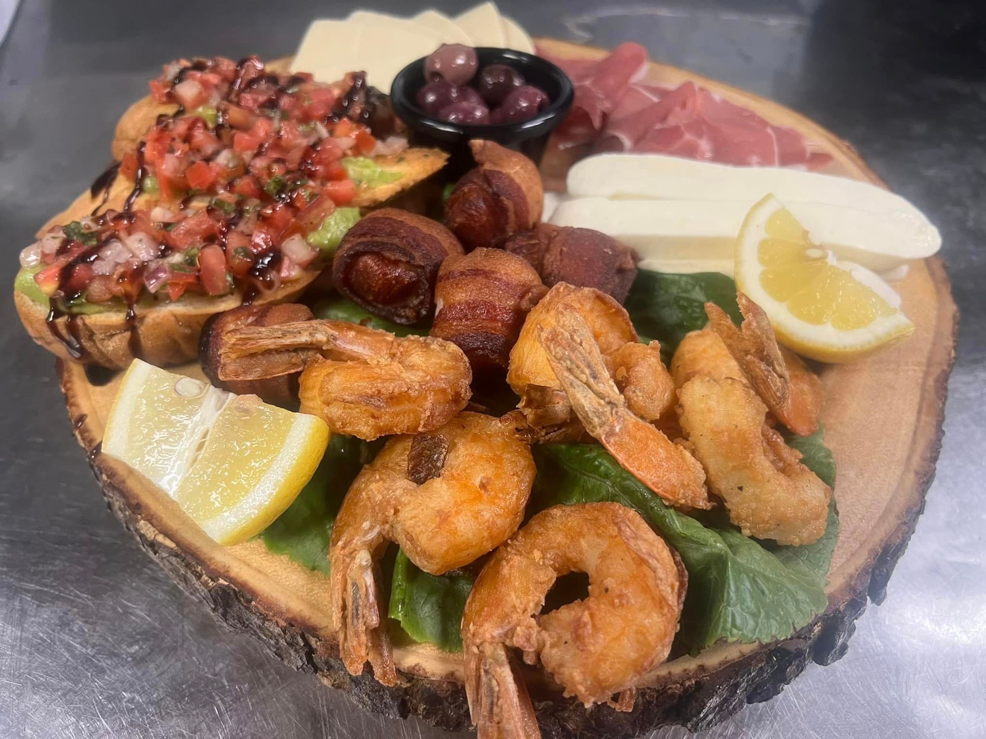 A wooden cutting board topped with fried shrimp , lemon slices , bacon and cheese.