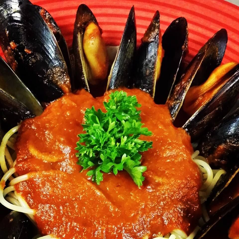 A plate of mussels and spaghetti with sauce and parsley on top