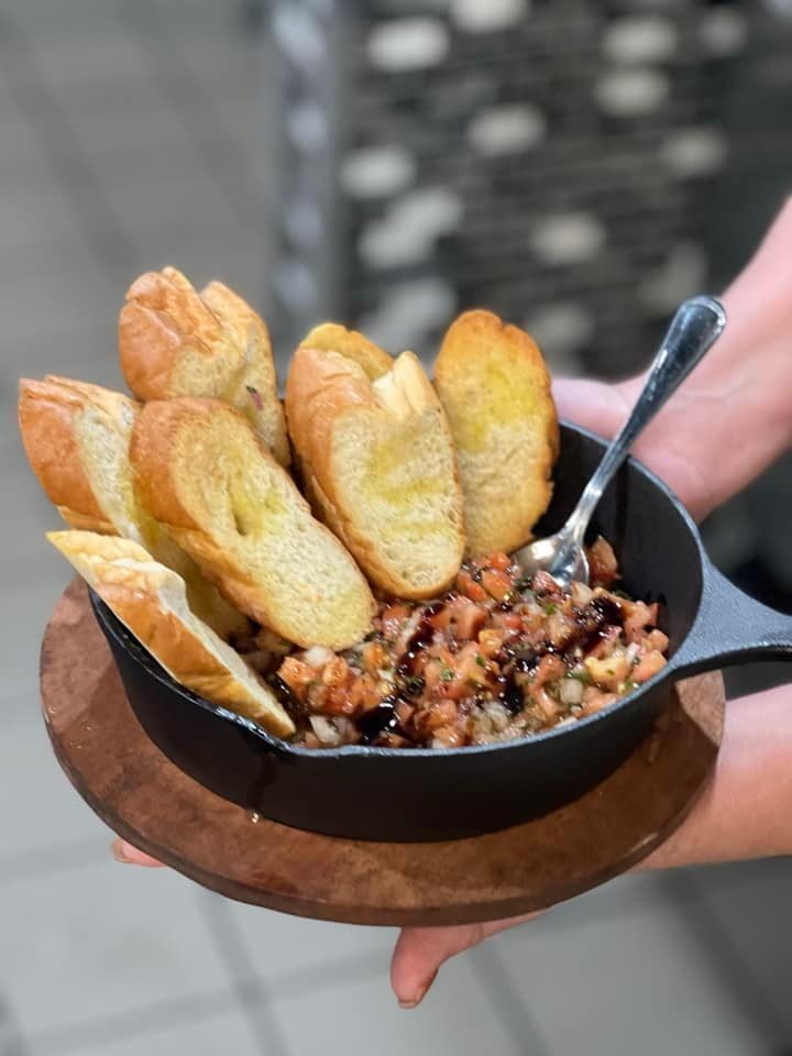 A person is holding a skillet of food with bread and a spoon in it.