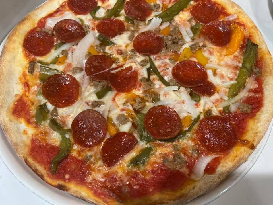 A pizza with pepperoni , cheese , peppers and sausage on a white plate.