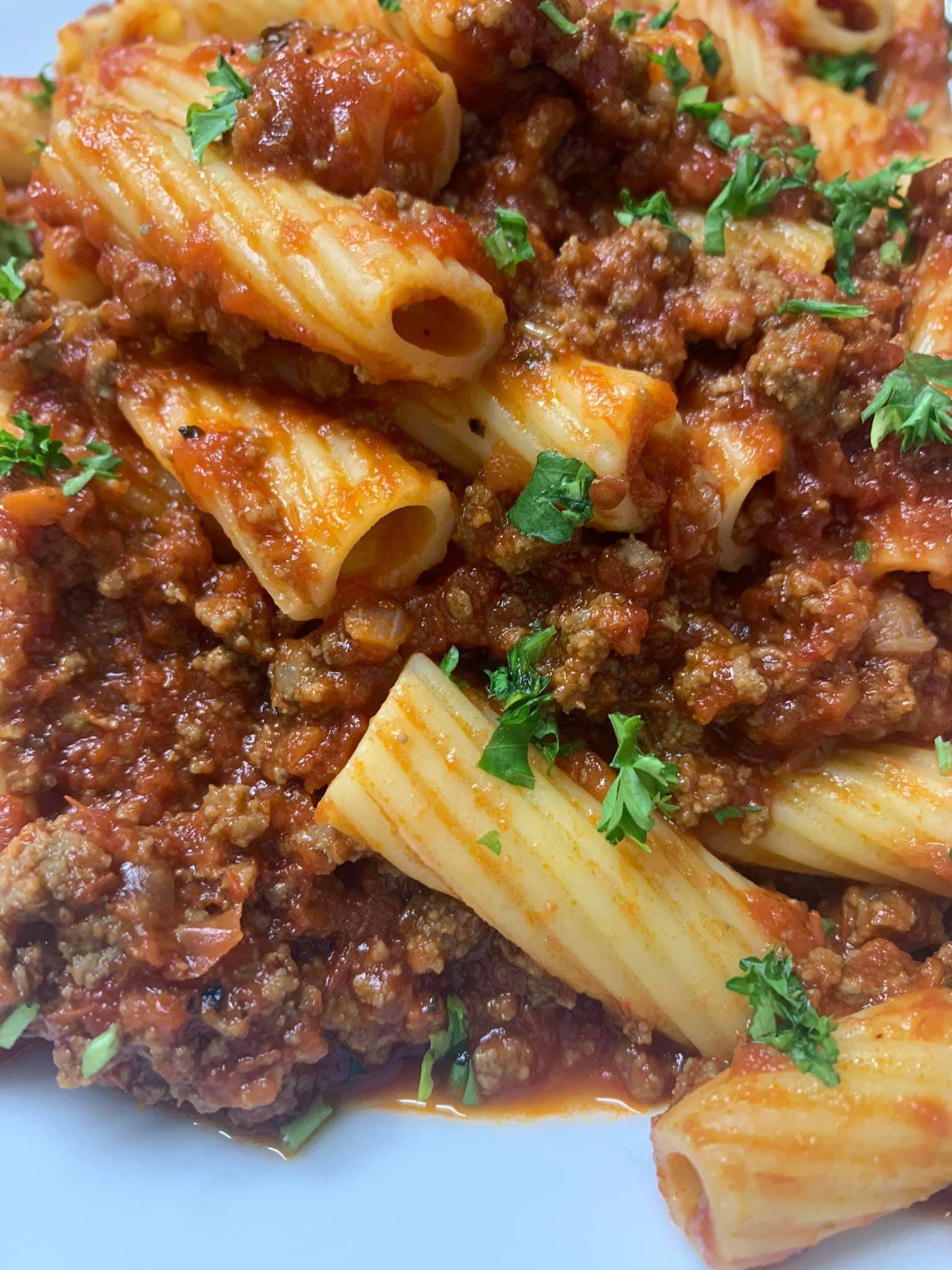 A close up of a plate of pasta with meat sauce and parsley.