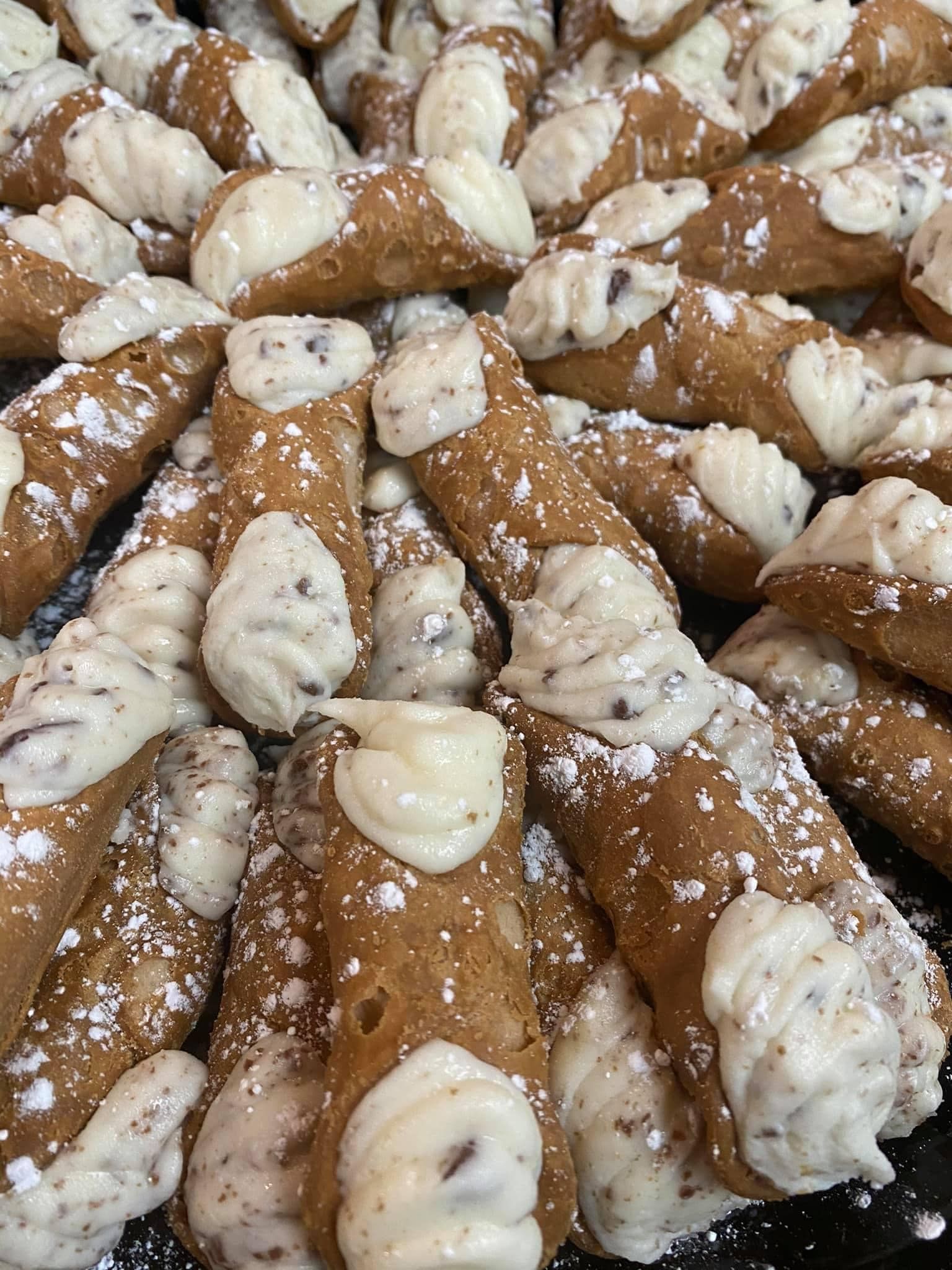 A bunch of cannoli with white frosting and powdered sugar on a table.