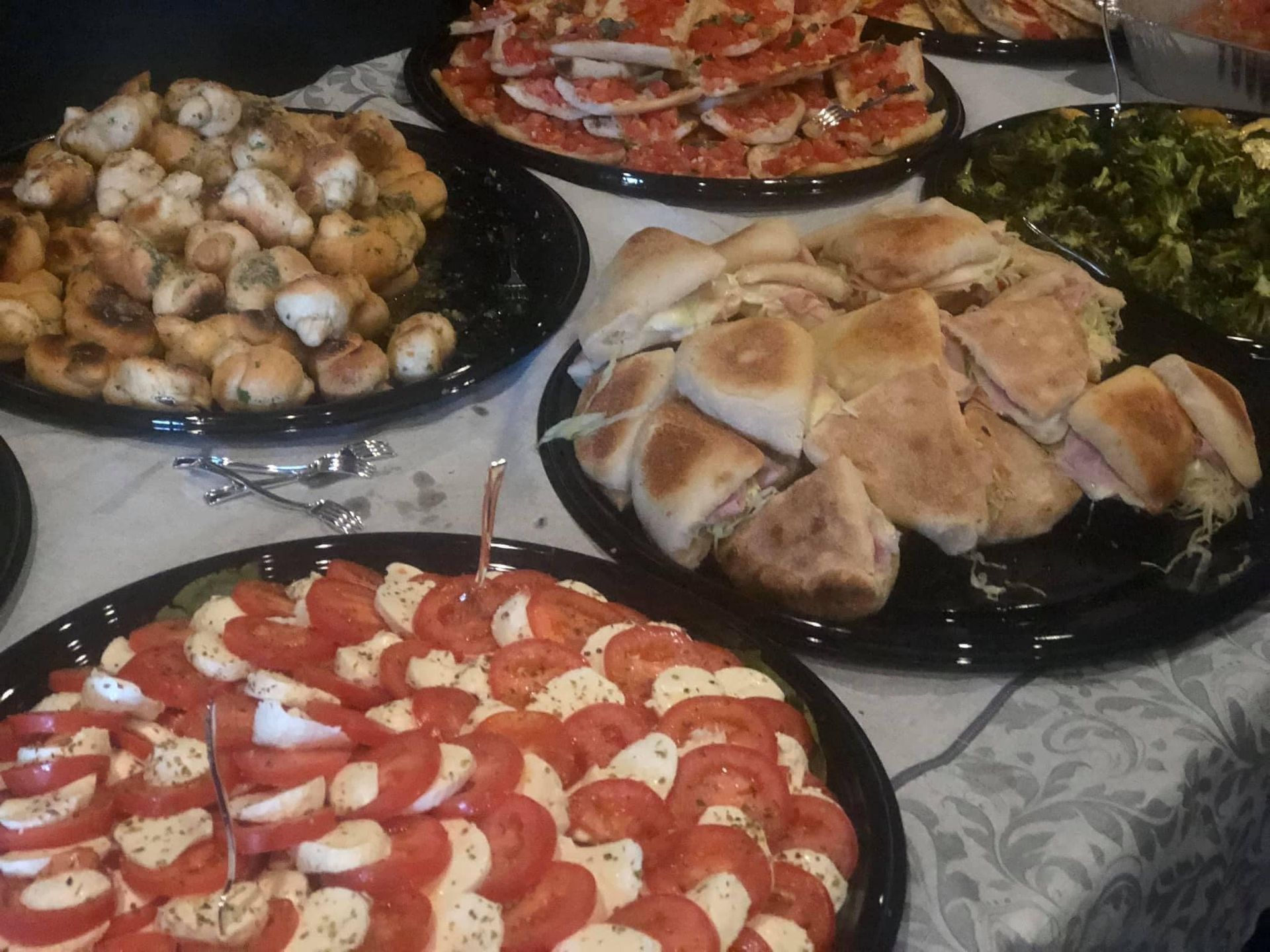Several plates of food are on a table including pizza and sandwiches