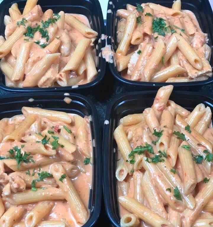 Four containers of pasta with sauce and parsley on top