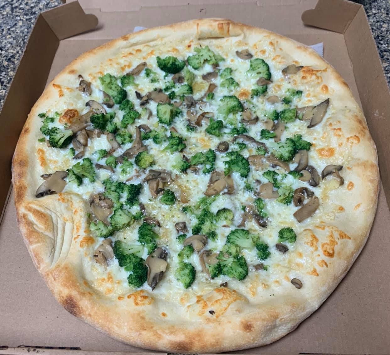 A pizza with broccoli , mushrooms and cheese is in a box.