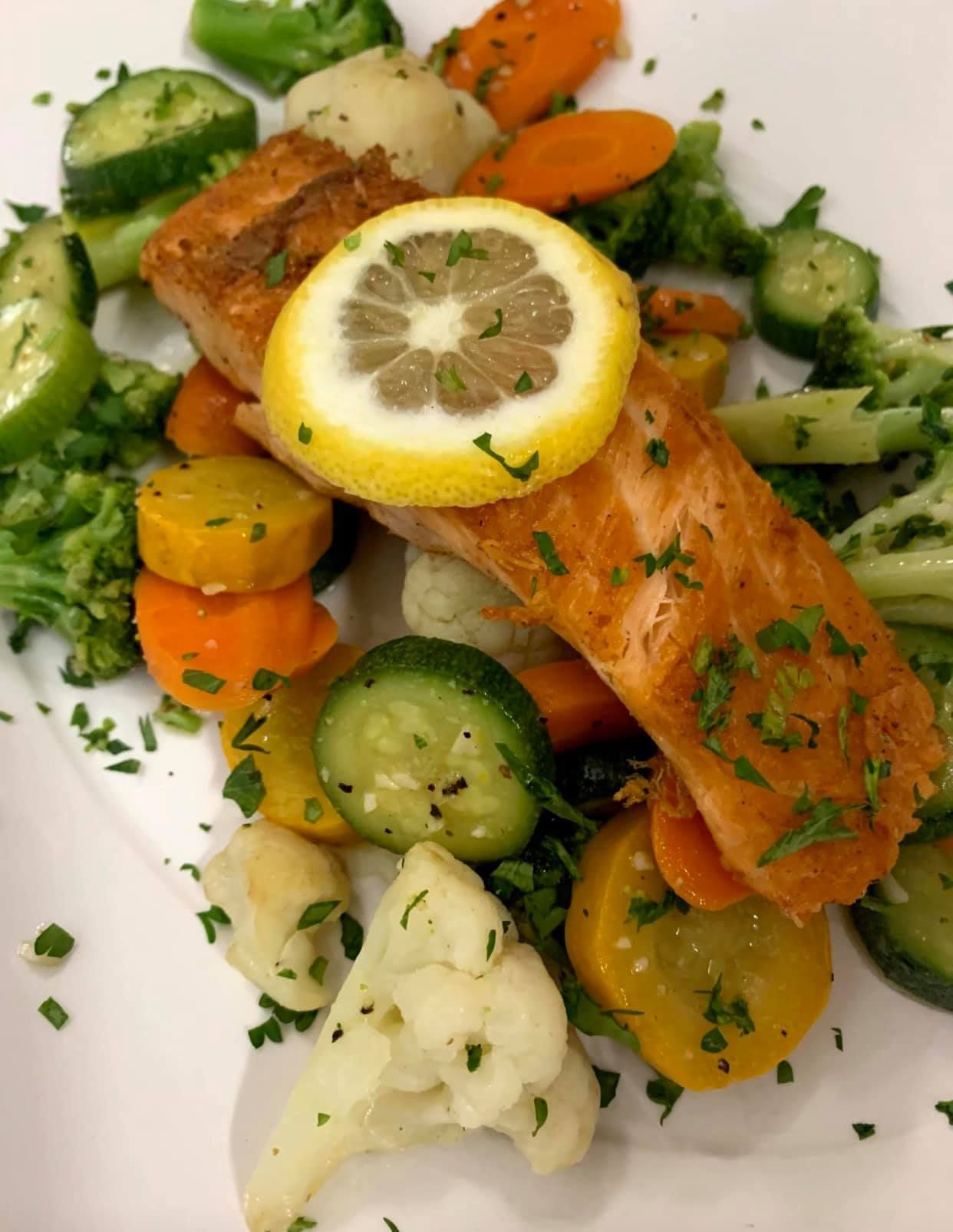 A white plate topped with salmon and vegetables with a lemon slice on top.