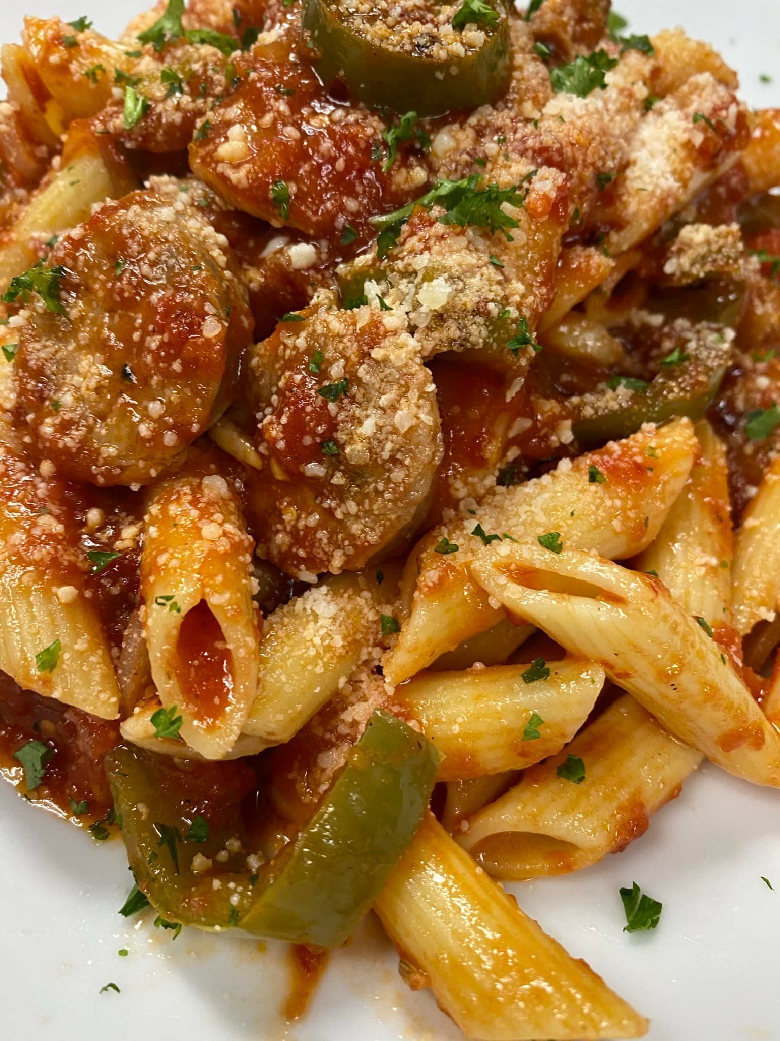 A close up of a plate of pasta with sauce and peppers on a table.