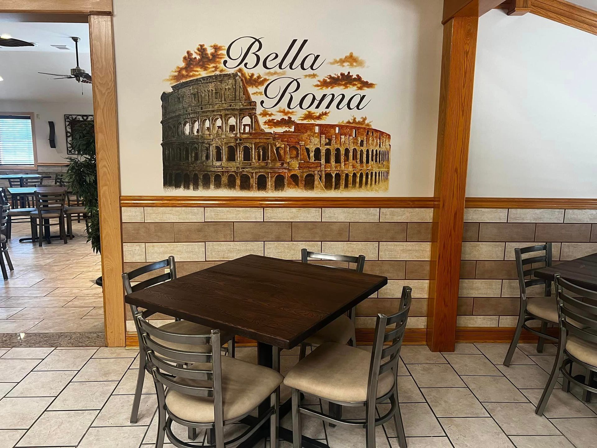 A restaurant with tables and chairs and a sign on the wall that says bella roma.