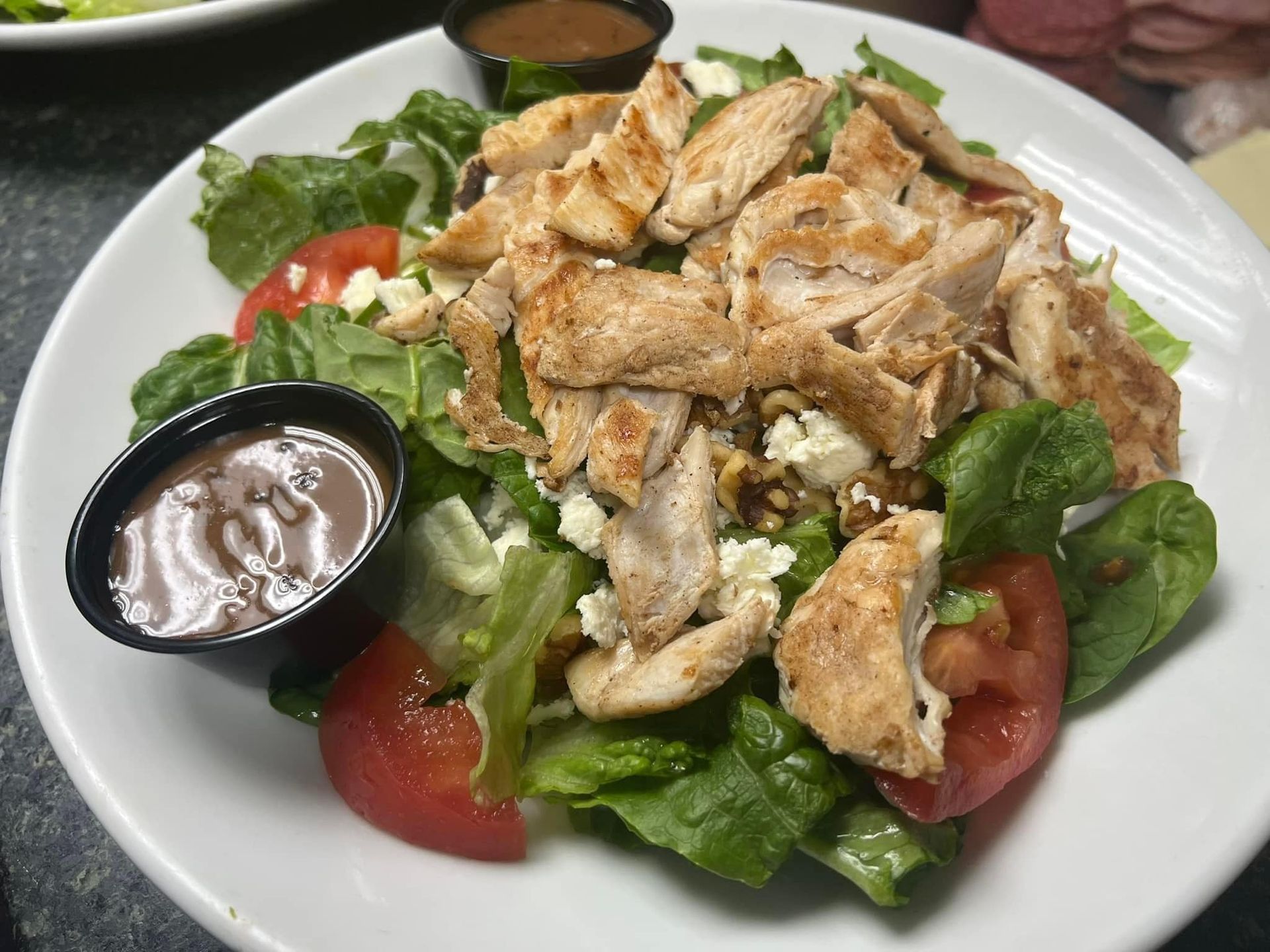 A white plate topped with a salad with chicken and tomatoes