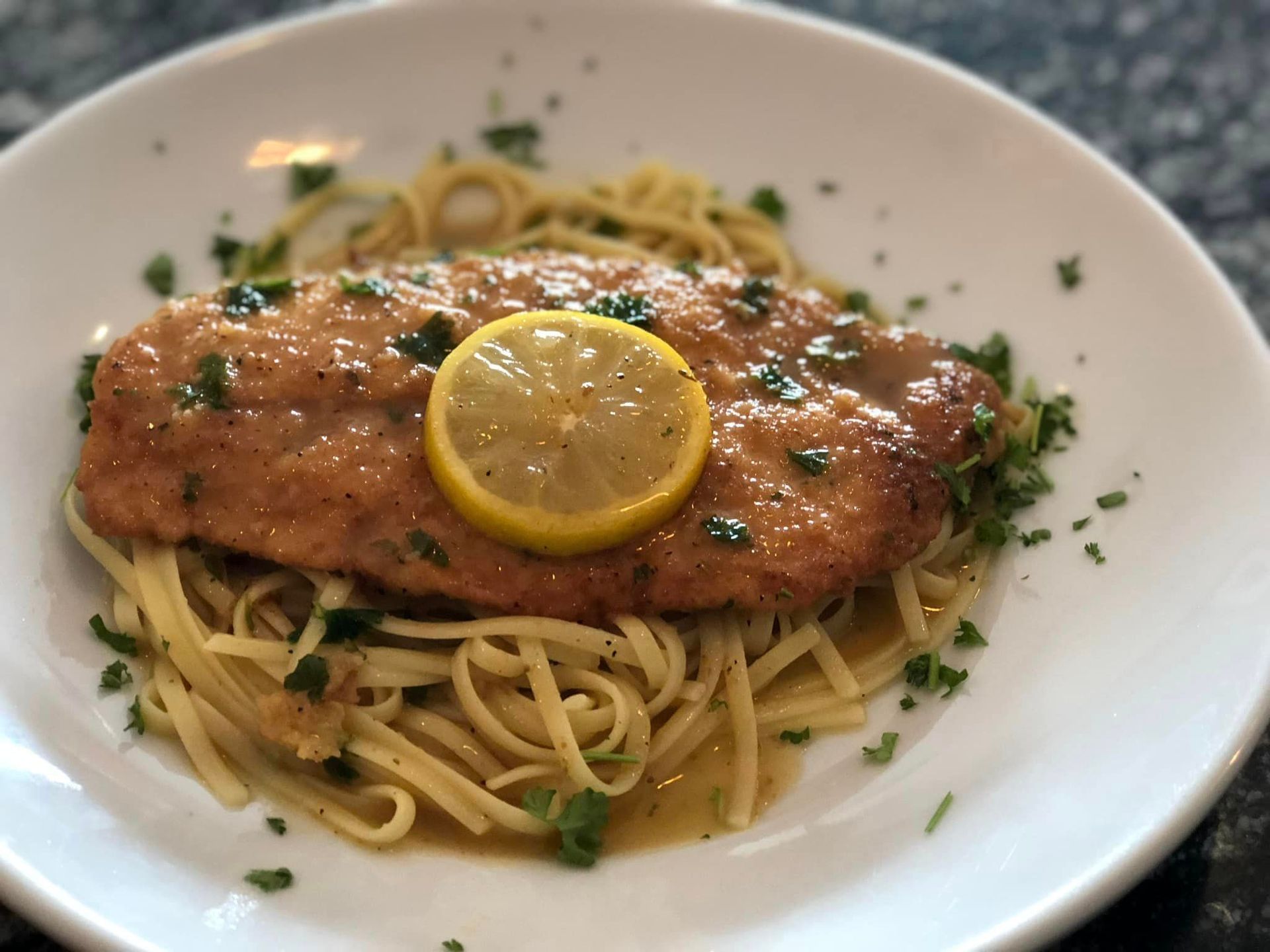 A white plate topped with chicken and noodles with a lemon slice on top.
