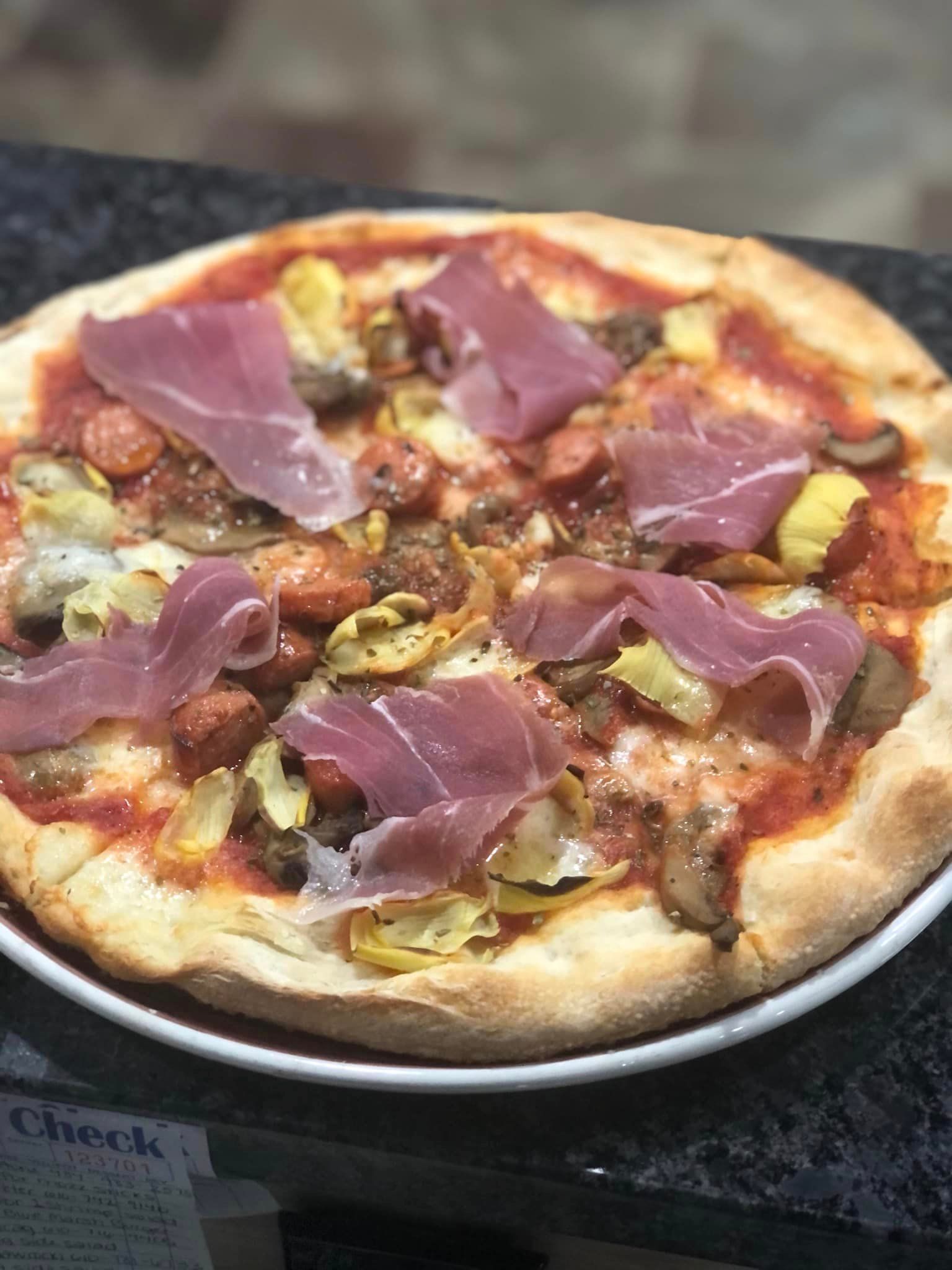 A pizza with meat and vegetables on a white plate on a table.