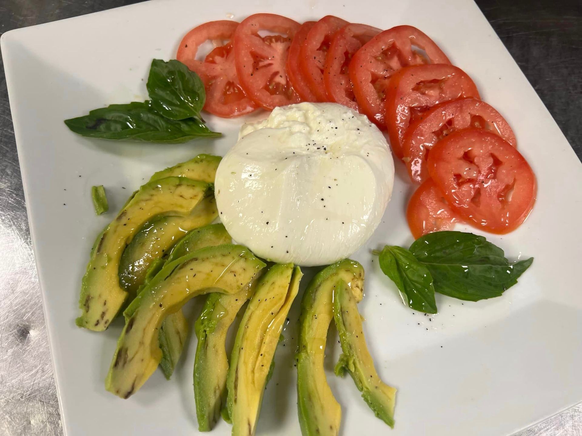 A white plate topped with sliced avocado , tomatoes and mozzarella.