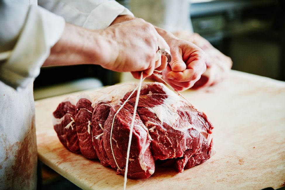 Un macellaio lega lo spago attorno a un grosso taglio di manzo crudo su un tagliere di legno.