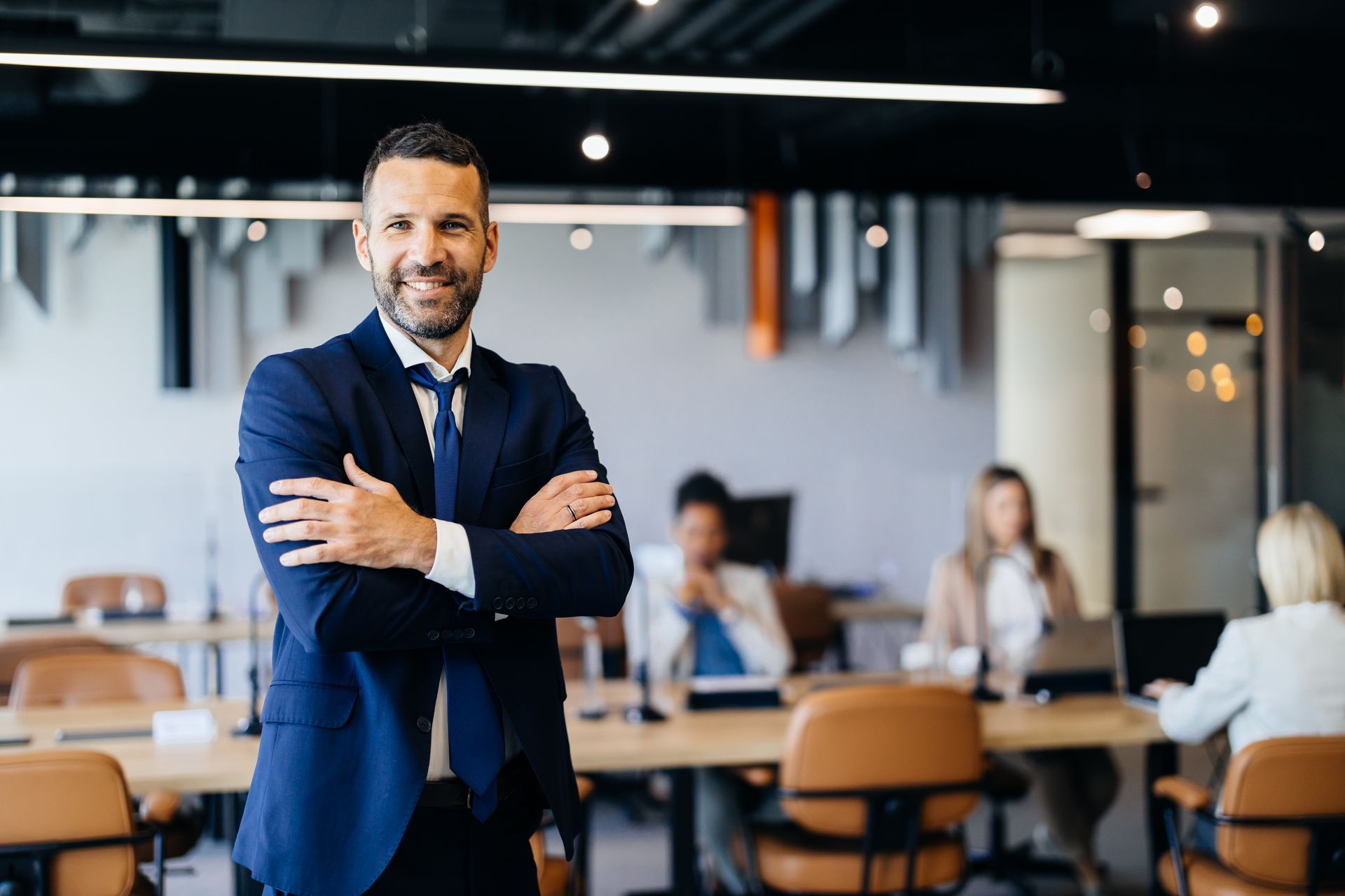 Tre impiegati seduti alla scrivania, uno sorridente, giacca blu, computer portatile, monitor, ufficio buio.