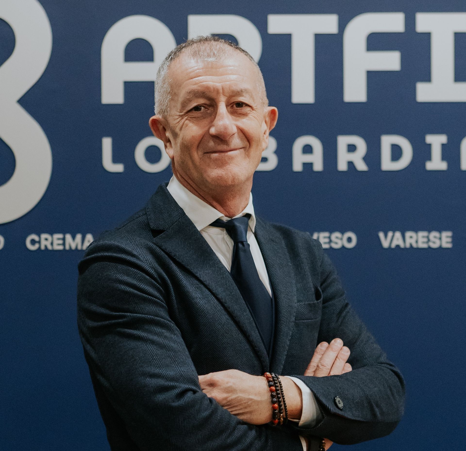 Uomo in giacca e cravatta su sfondo rosso, che guarda avanti.