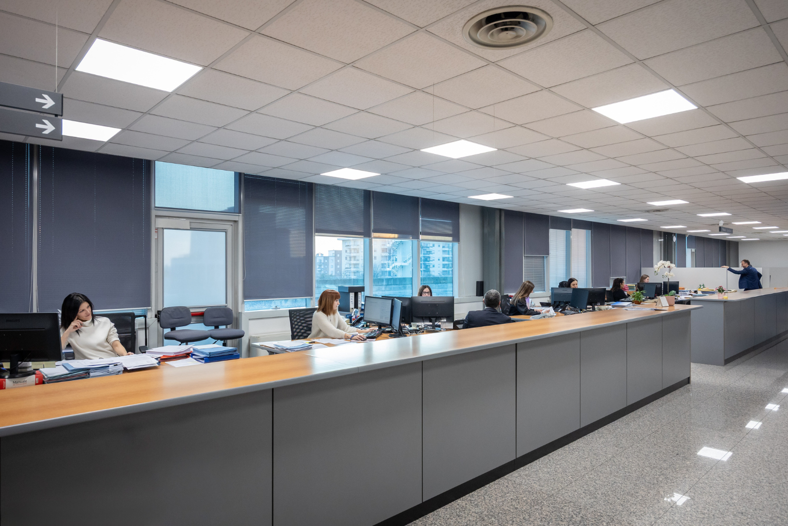 Un uomo in abito blu, con le braccia incrociate, sorride con sicurezza in un ufficio. Sullo sfondo, un team che lavora.