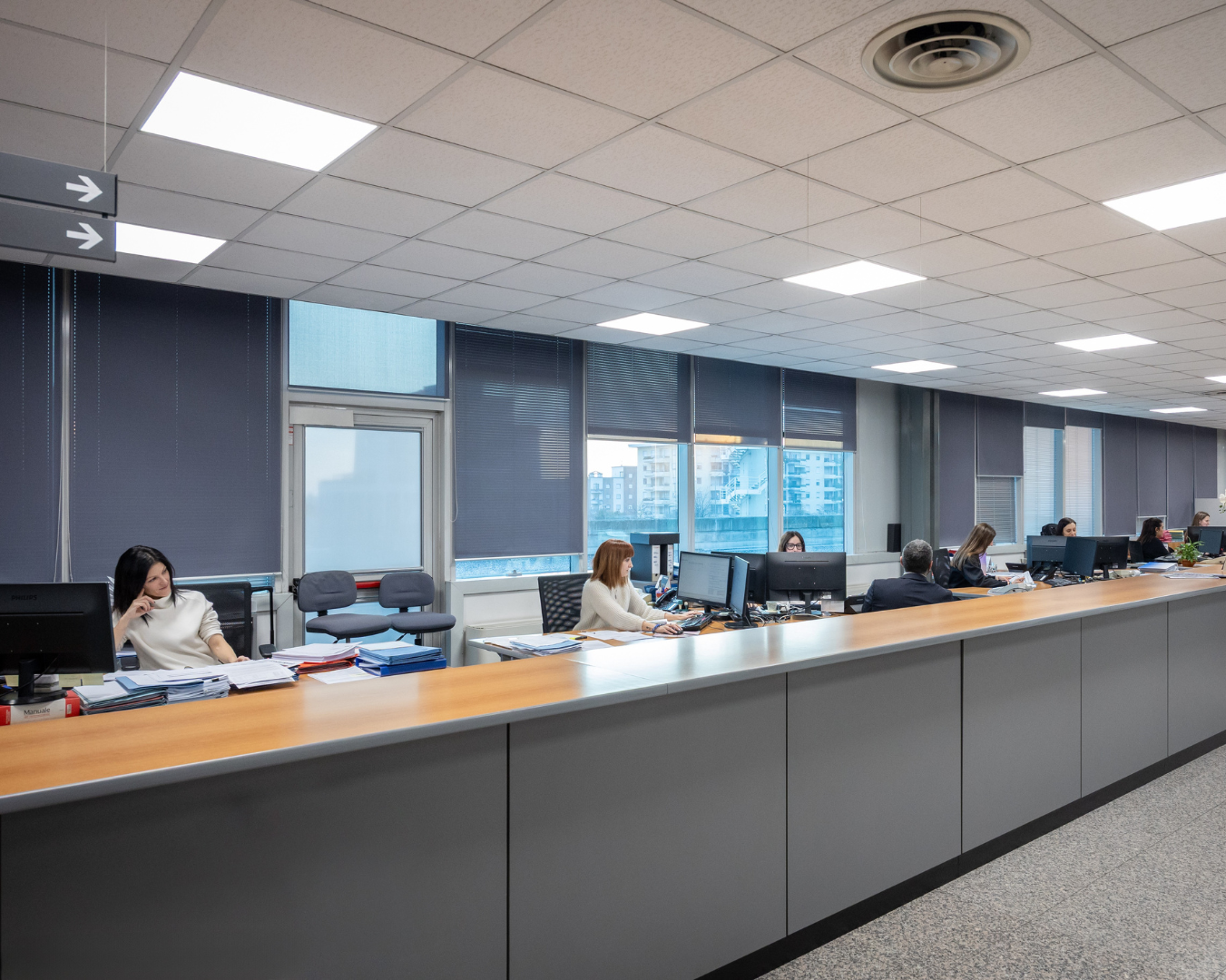 Una persona con una camicia azzurra punta la penna verso documenti finanziari vicino a una calcolatrice su una scrivania.