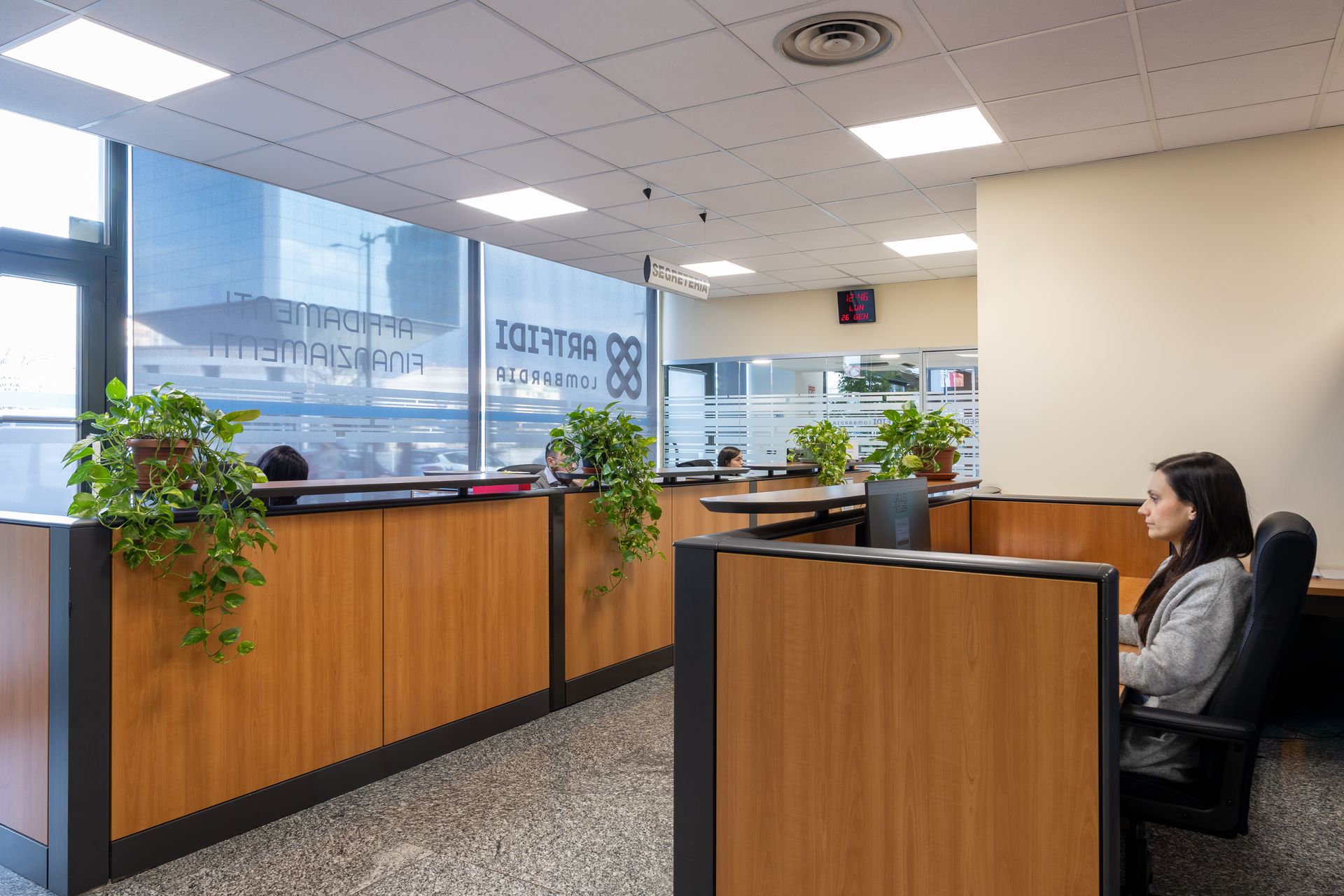 Tre impiegati seduti alla scrivania, uno sorridente, giacca blu, computer portatile, monitor, ufficio buio.