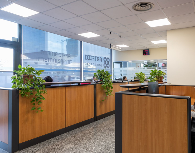 Una persona con una camicia azzurra punta la penna verso documenti finanziari vicino a una calcolatrice su una scrivania.