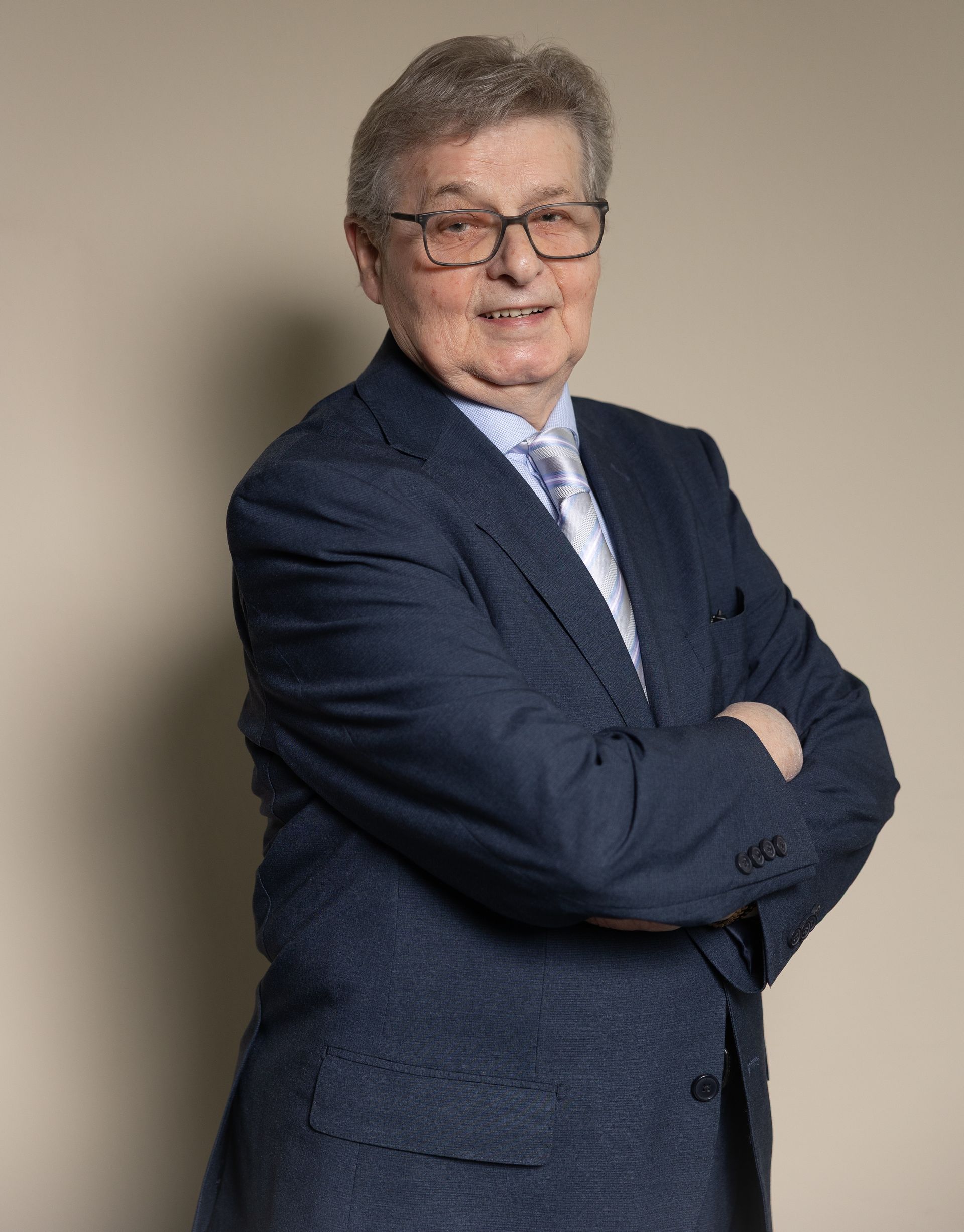 Uomo in giacca e cravatta su sfondo rosso; guarda direttamente l'osservatore.