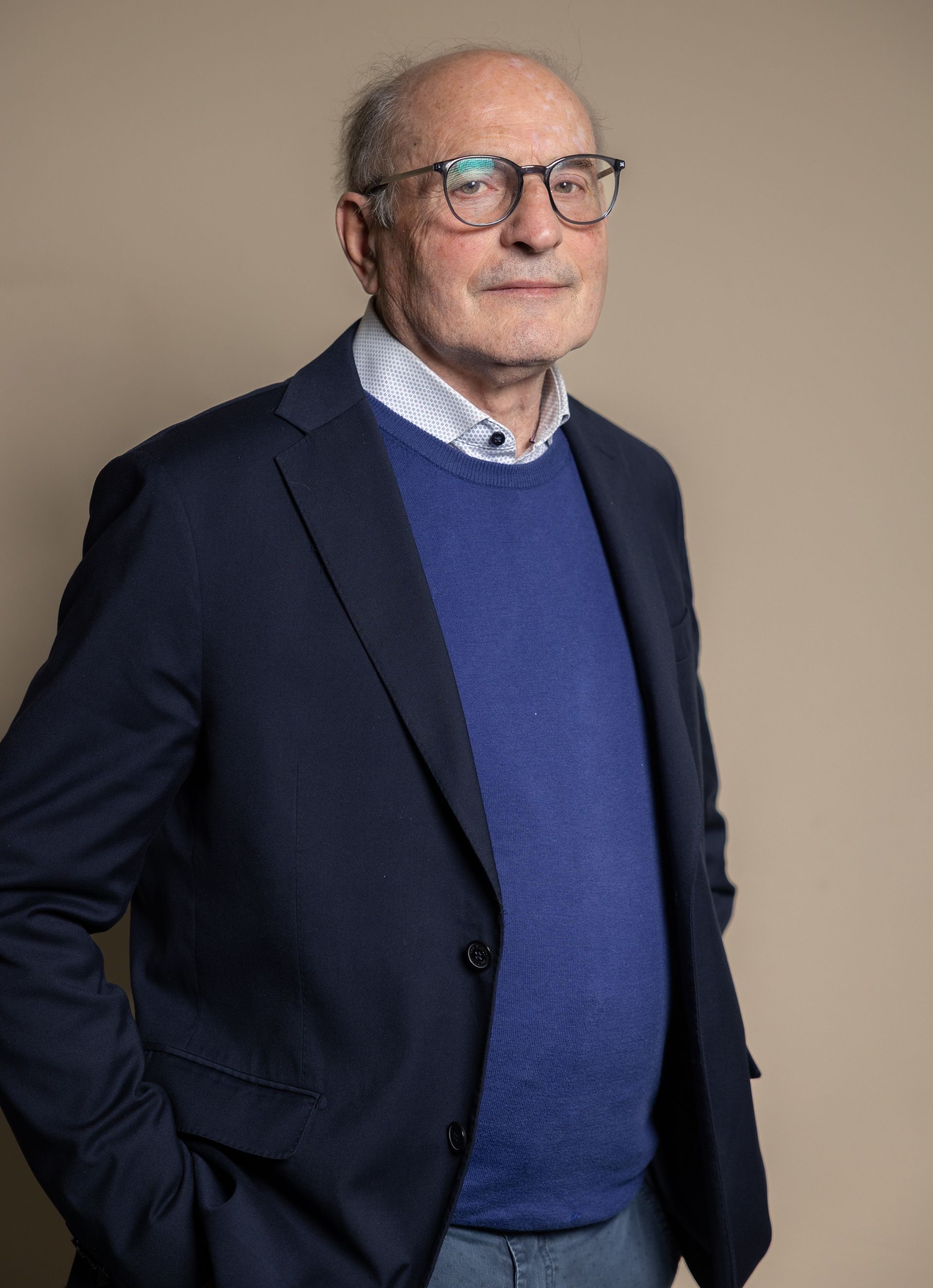 Uomo con gli occhiali, sorridente, che indossa un maglione e una cravatta, su sfondo rosso.