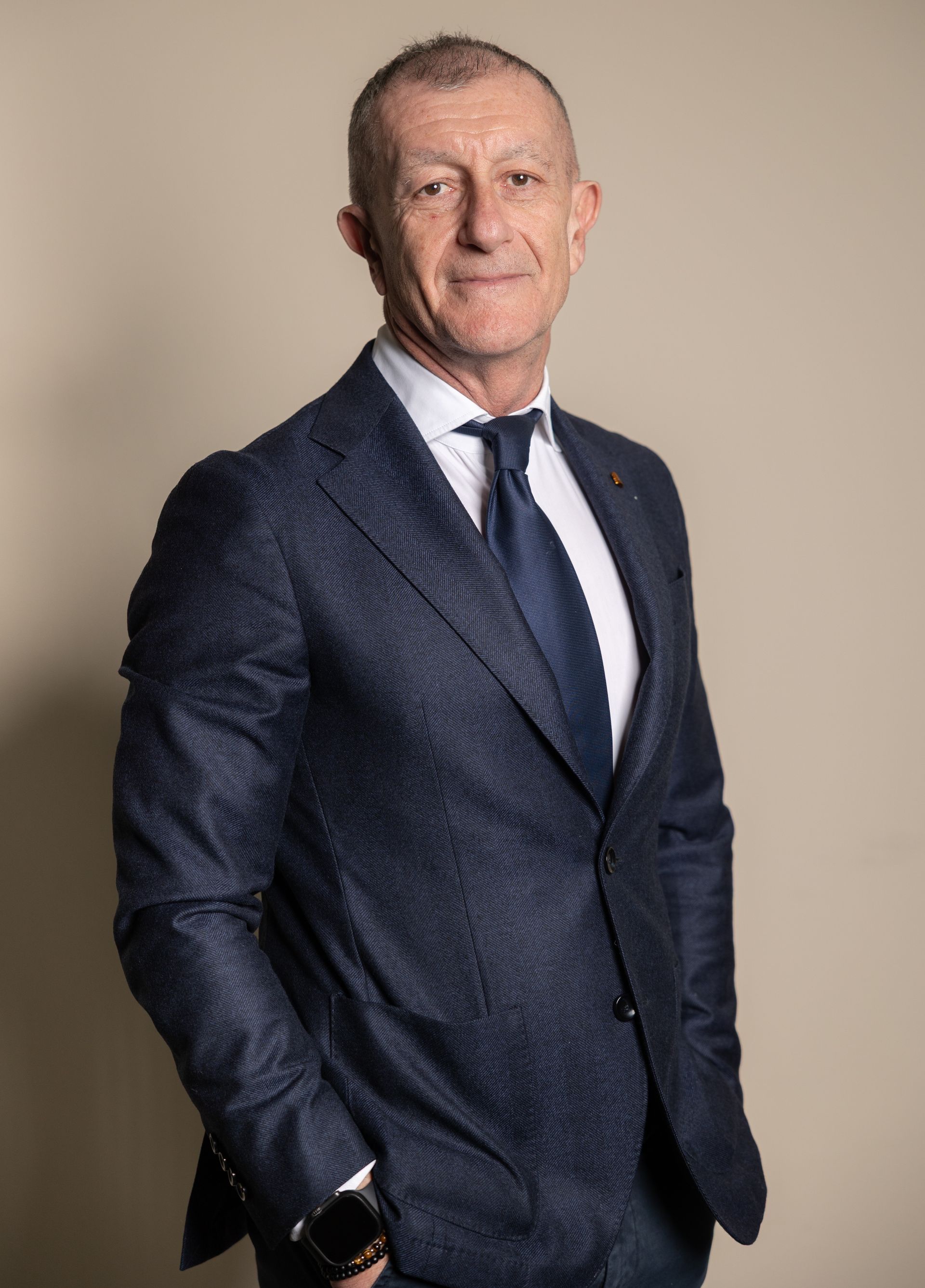 Uomo in giacca e cravatta su sfondo rosso, che guarda avanti.