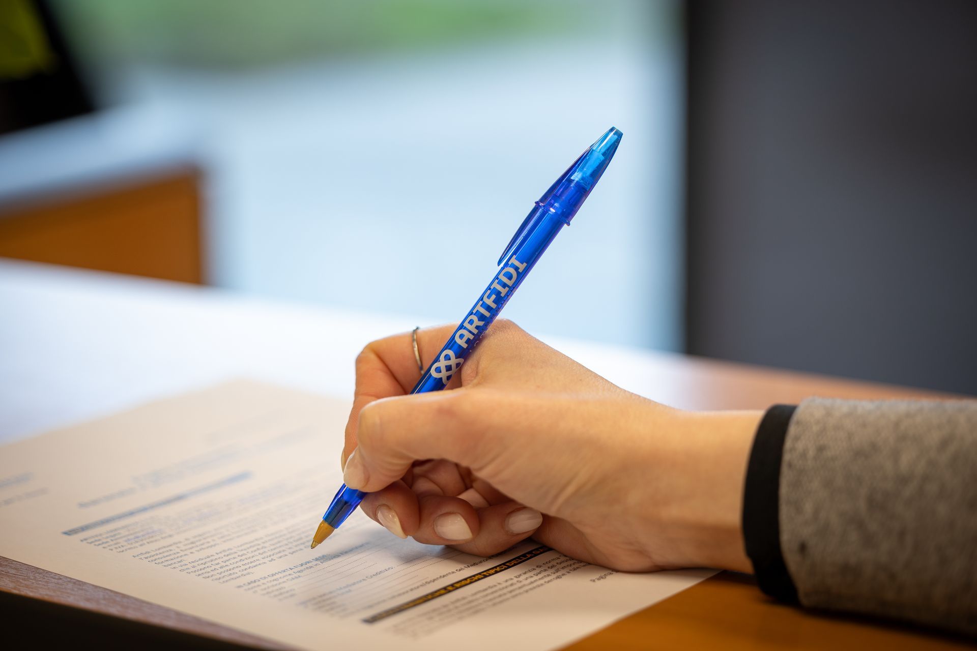 Una persona con una camicia azzurra punta la penna verso documenti finanziari vicino a una calcolatrice su una scrivania.