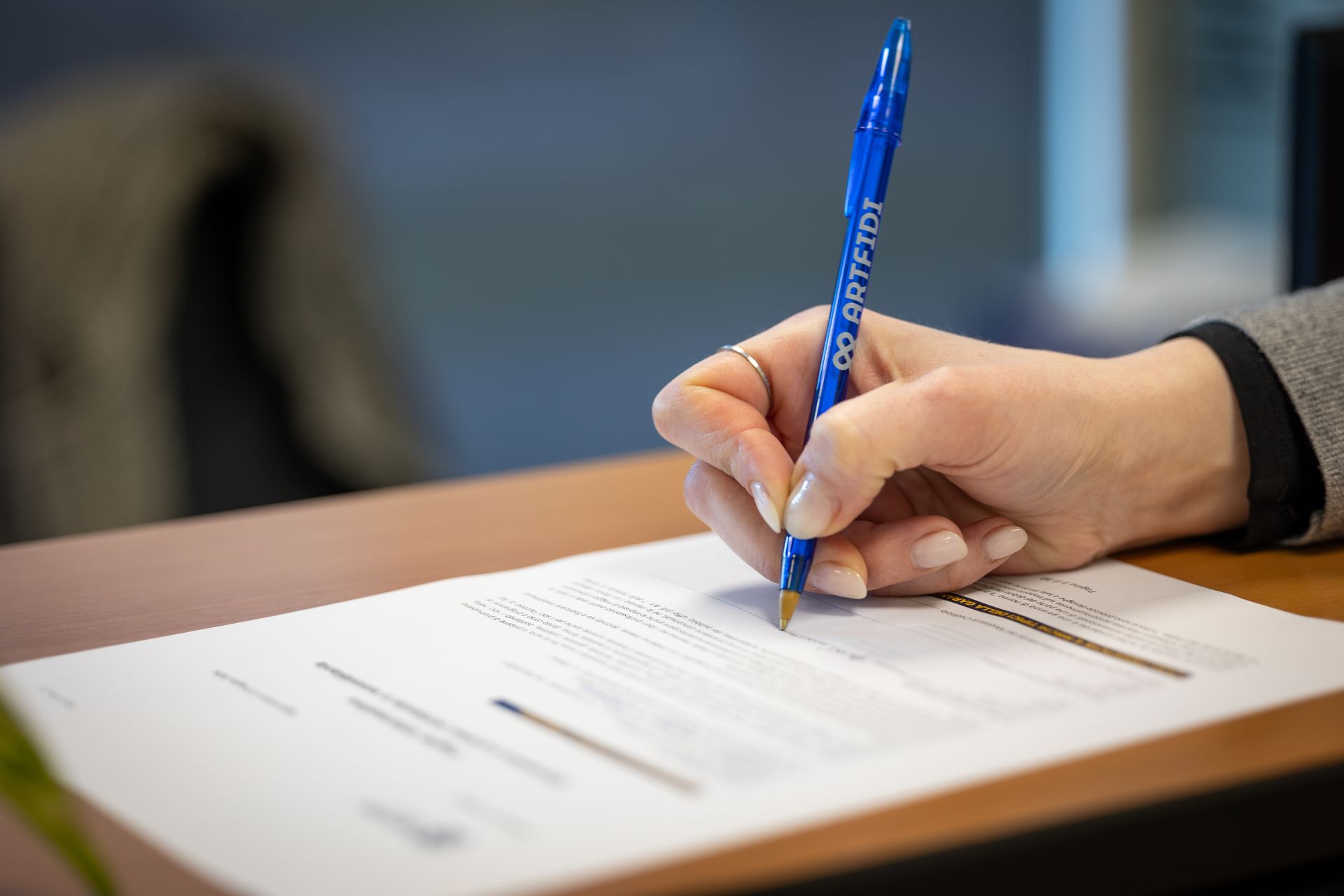 Una persona con una camicia blu esamina documenti finanziari con una penna alla scrivania. È visibile una calcolatrice.