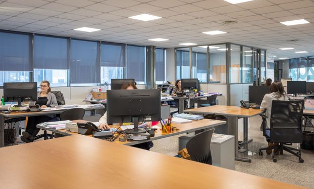 Tre impiegati seduti alla scrivania, uno sorridente, giacca blu, computer portatile, monitor, ufficio buio.