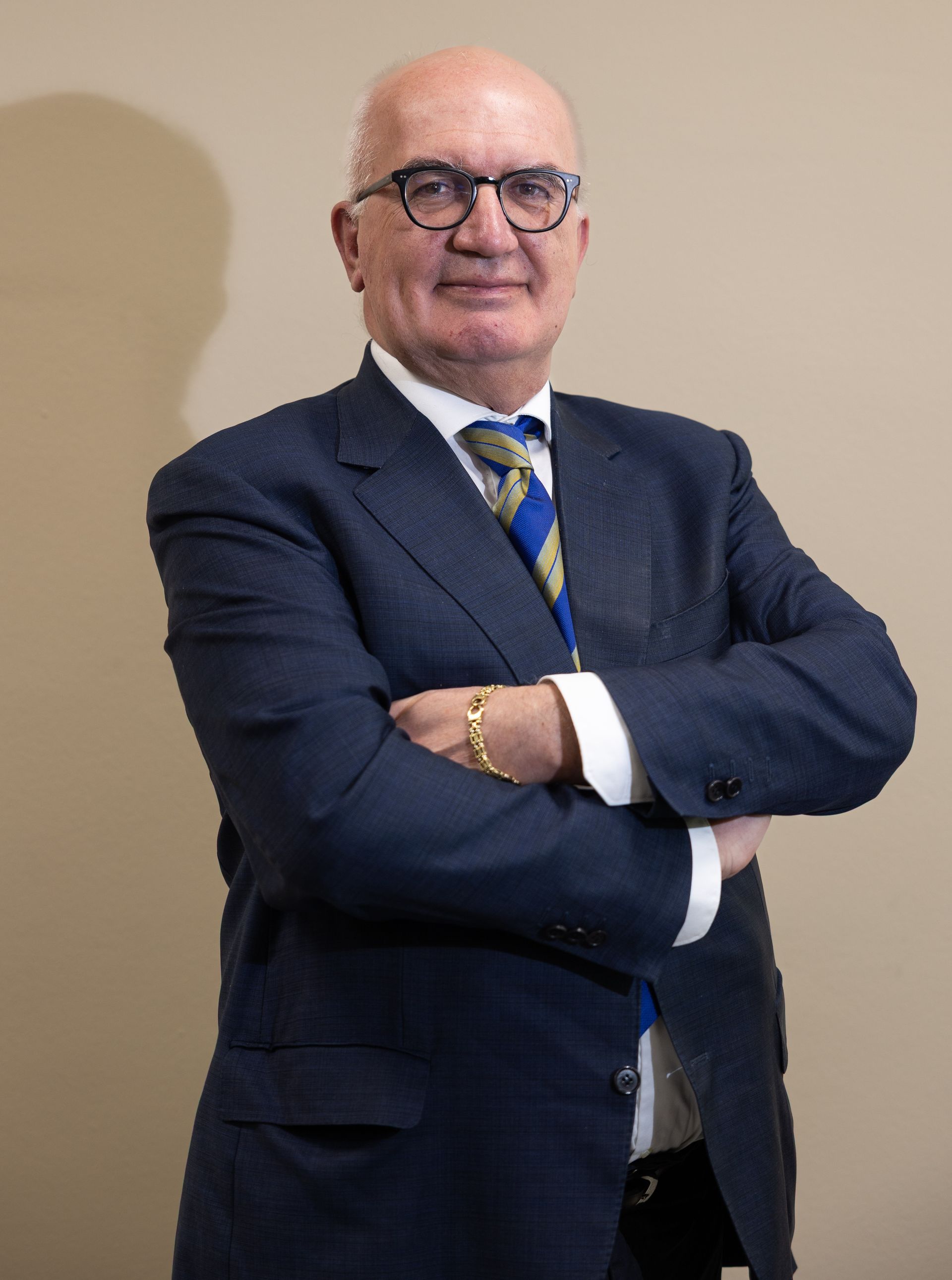 Uomo con occhiali e barba, in abito su sfondo rosso, sorridente.