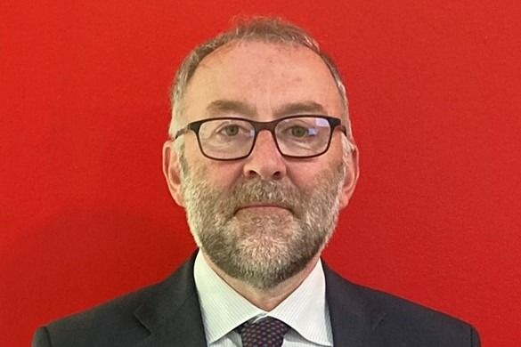 Uomo con occhiali e barba che indossa un abito, su uno sfondo rosso.