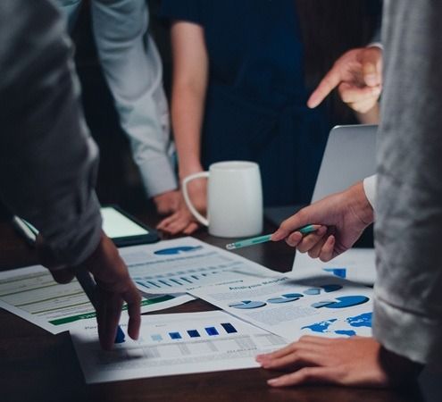 Persone sedute a un tavolo che analizzano i resoconti finanziari, indicando grafici e tabelle.