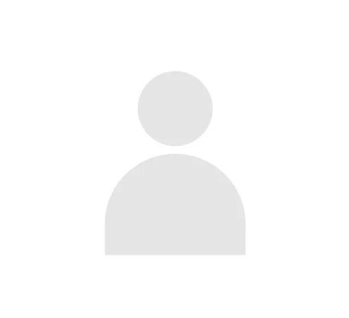 Uomo con barba e capelli grigi, vestito in giacca e cravatta, sorridente su sfondo rosso.