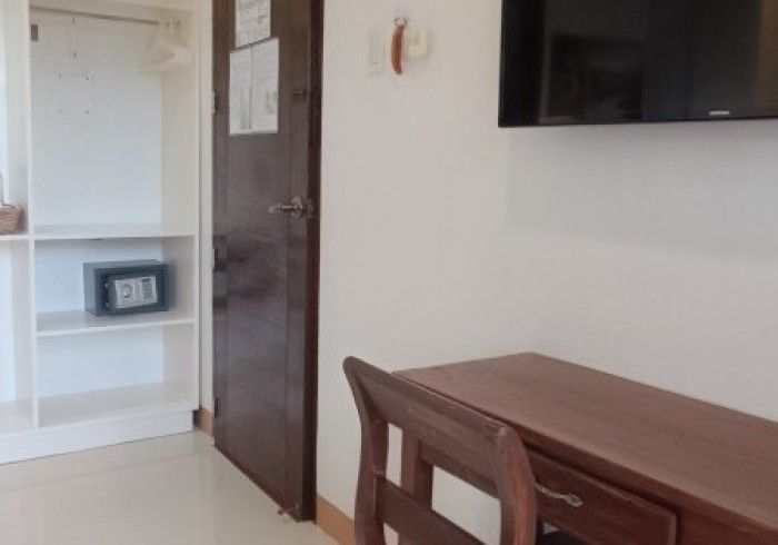 A room with a desk and chair and a television on the wall.