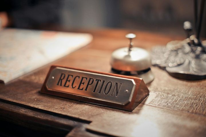 A reception sign is on a wooden table next to a bell.