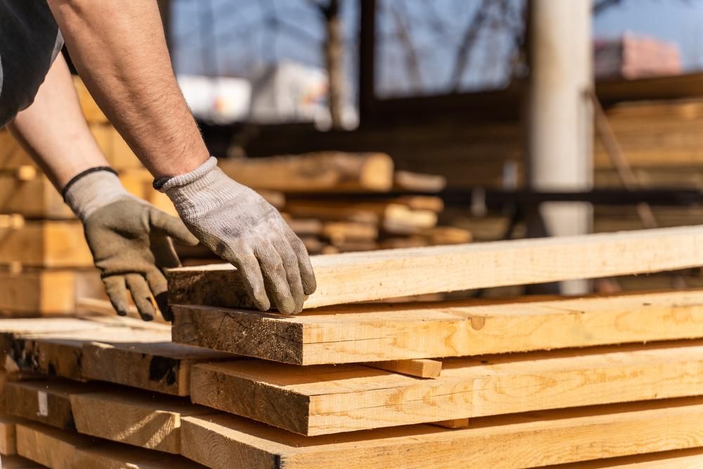 A Man Wearing Gloves Is Stacking Wooden Boards on Top of Each Other — Budget Timbers in North Lismore, NSW
