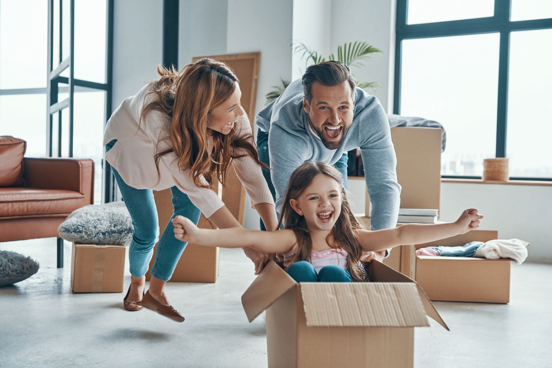 A family is playing with a little girl in a cardboard box.